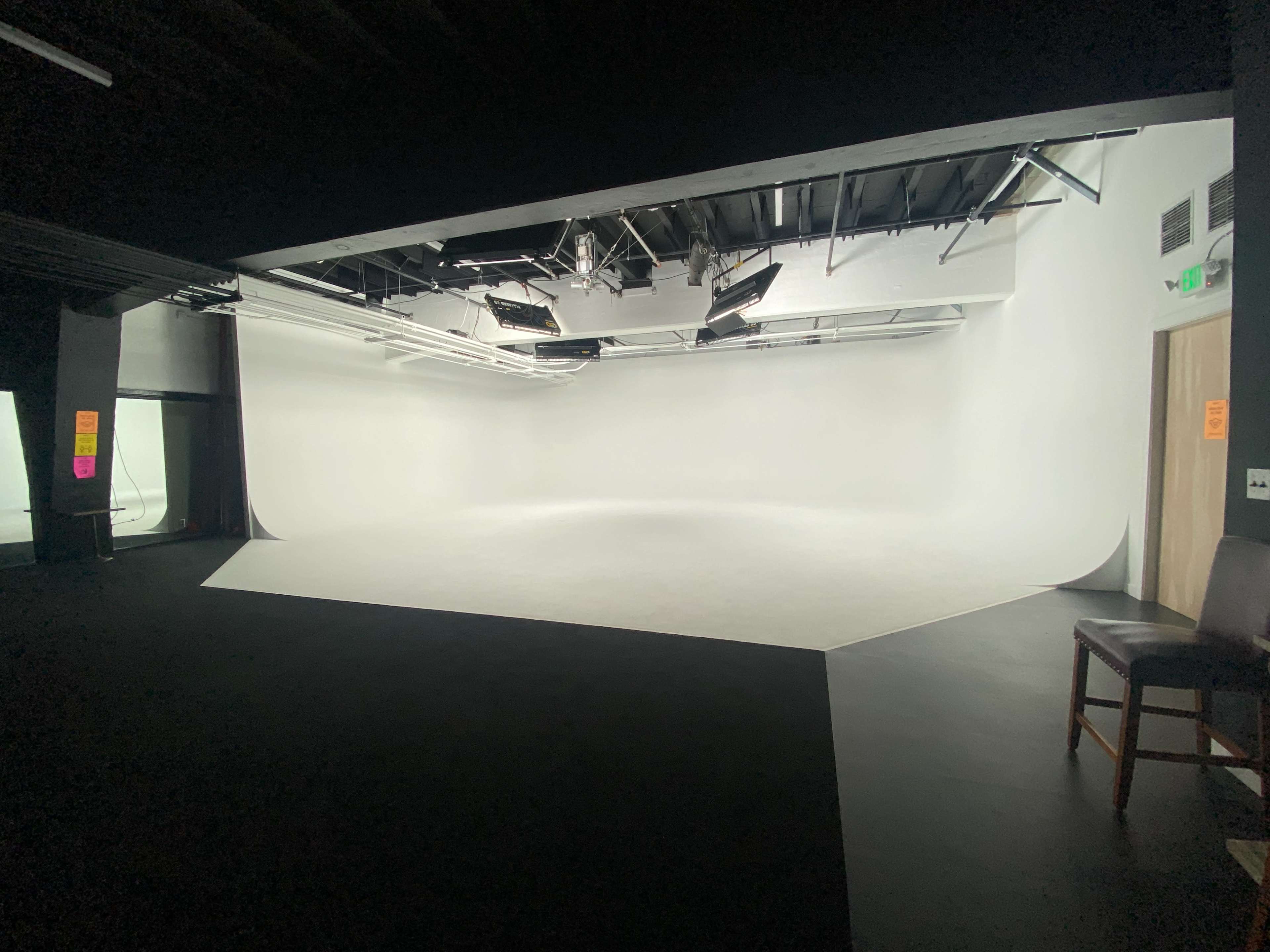 An empty photography studio with a seamless white backdrop and overhead lighting.