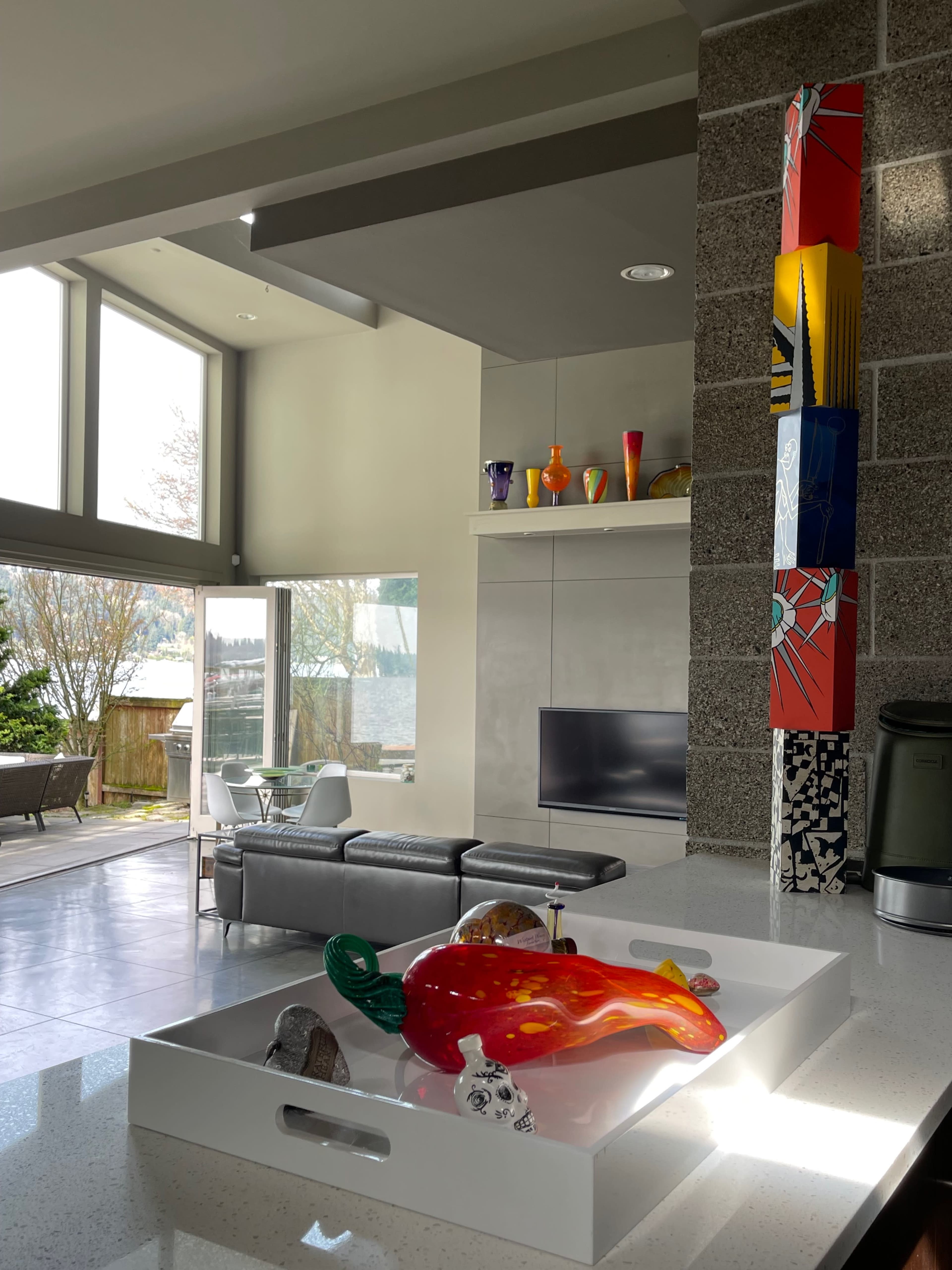 A modern kitchen with a colorful glass centerpiece and large windows showcasing a view of a lake and outdoor seating area.