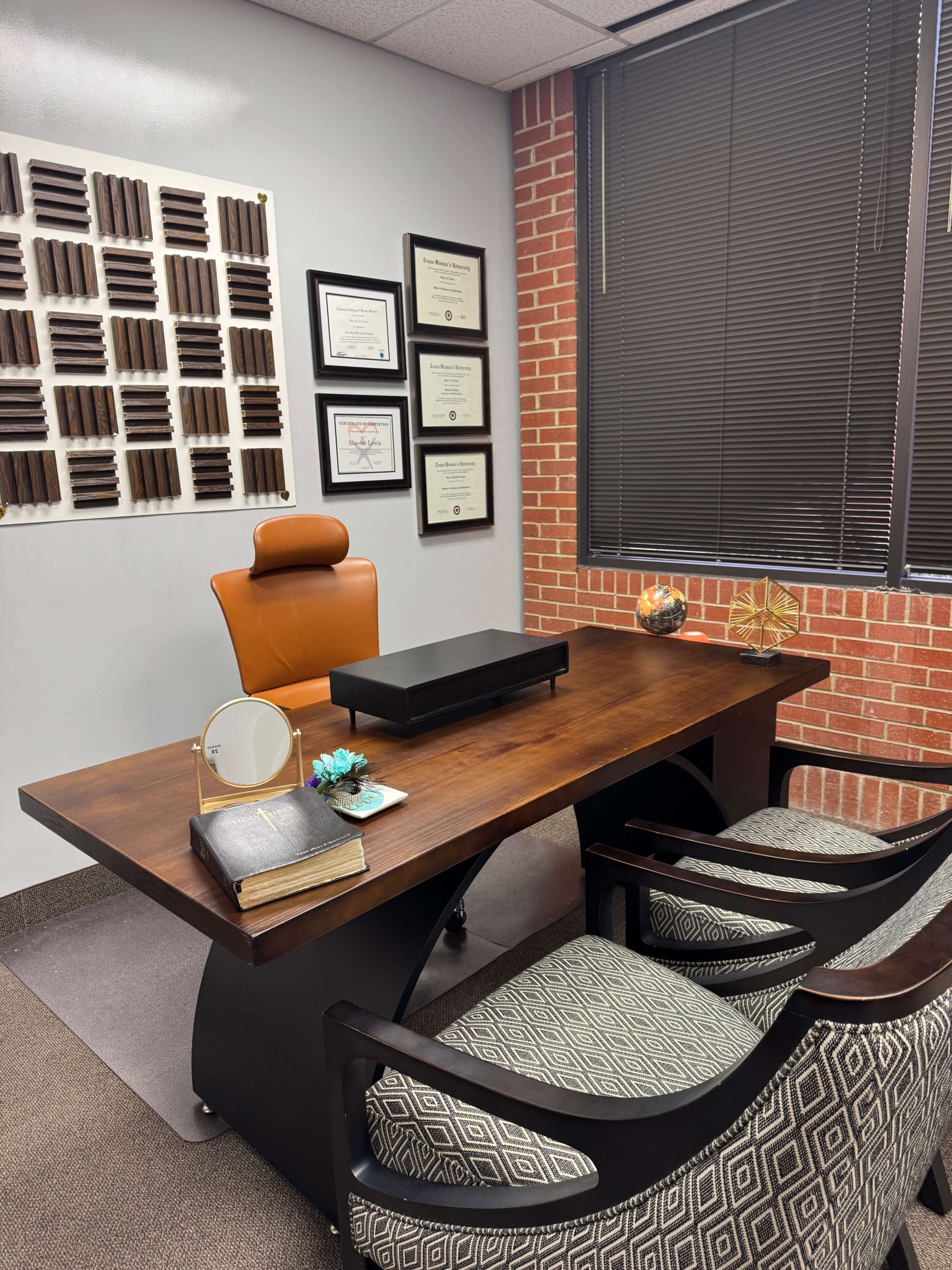 The image shows a modern office with a wooden desk, two patterned chairs, a wall adorned with framed certificates, and soundproofing panels.