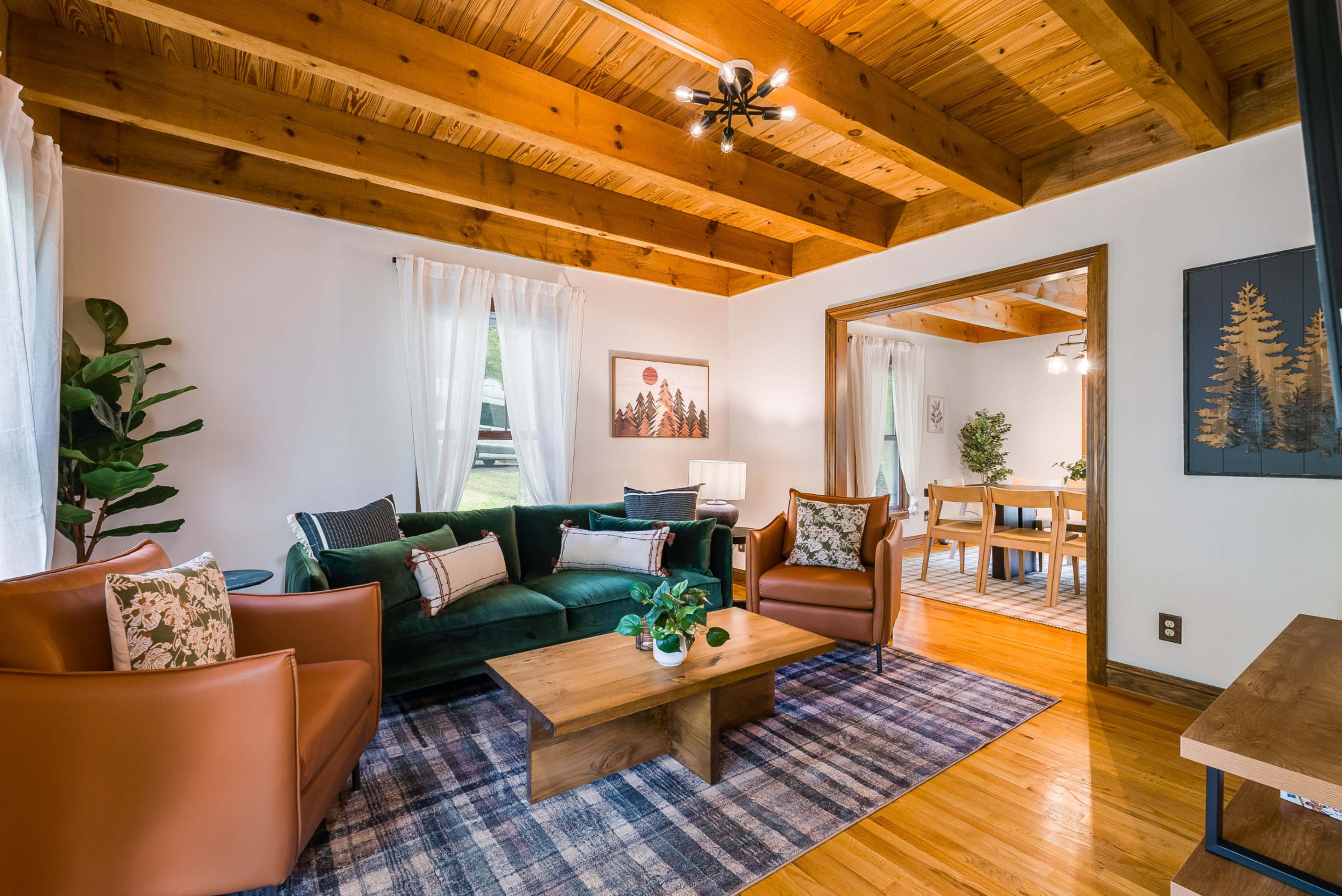 The image shows a cozy living room with wooden beams, a green sofa, and two brown armchairs, accompanied by a coffee table and a patterned rug.