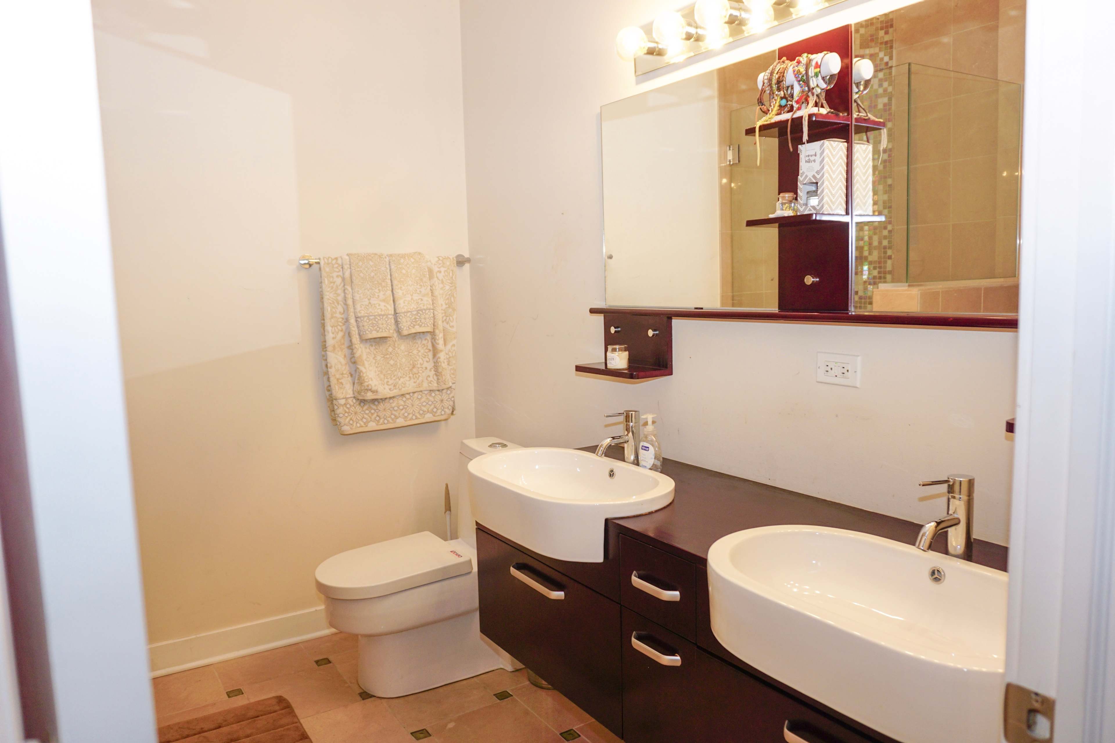 A modern bathroom with dual sinks, a wall-mounted mirror, and a toilet prominently displayed.