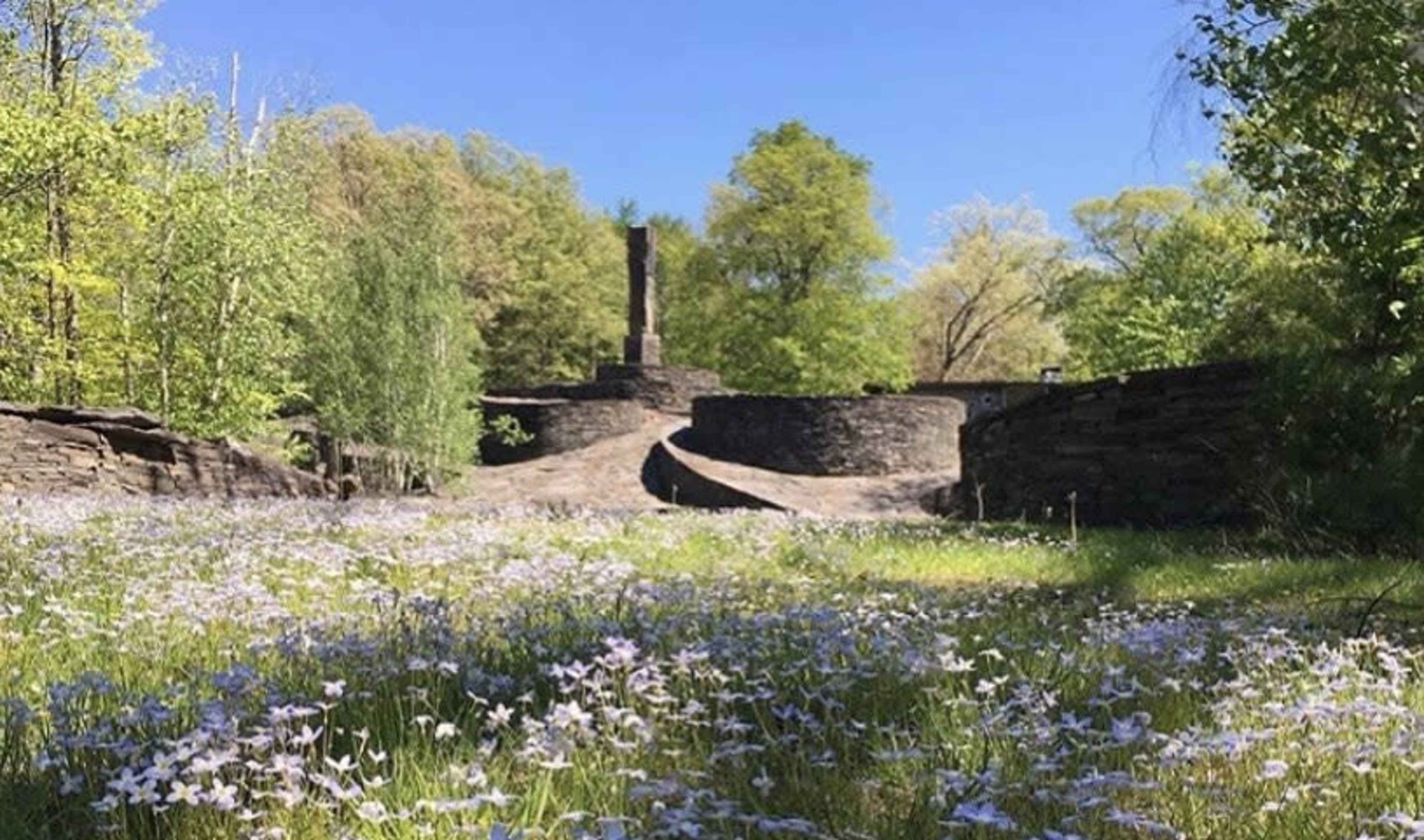 A stone memorial stands amid a landscaped area with a field of wildflowers in the foreground.