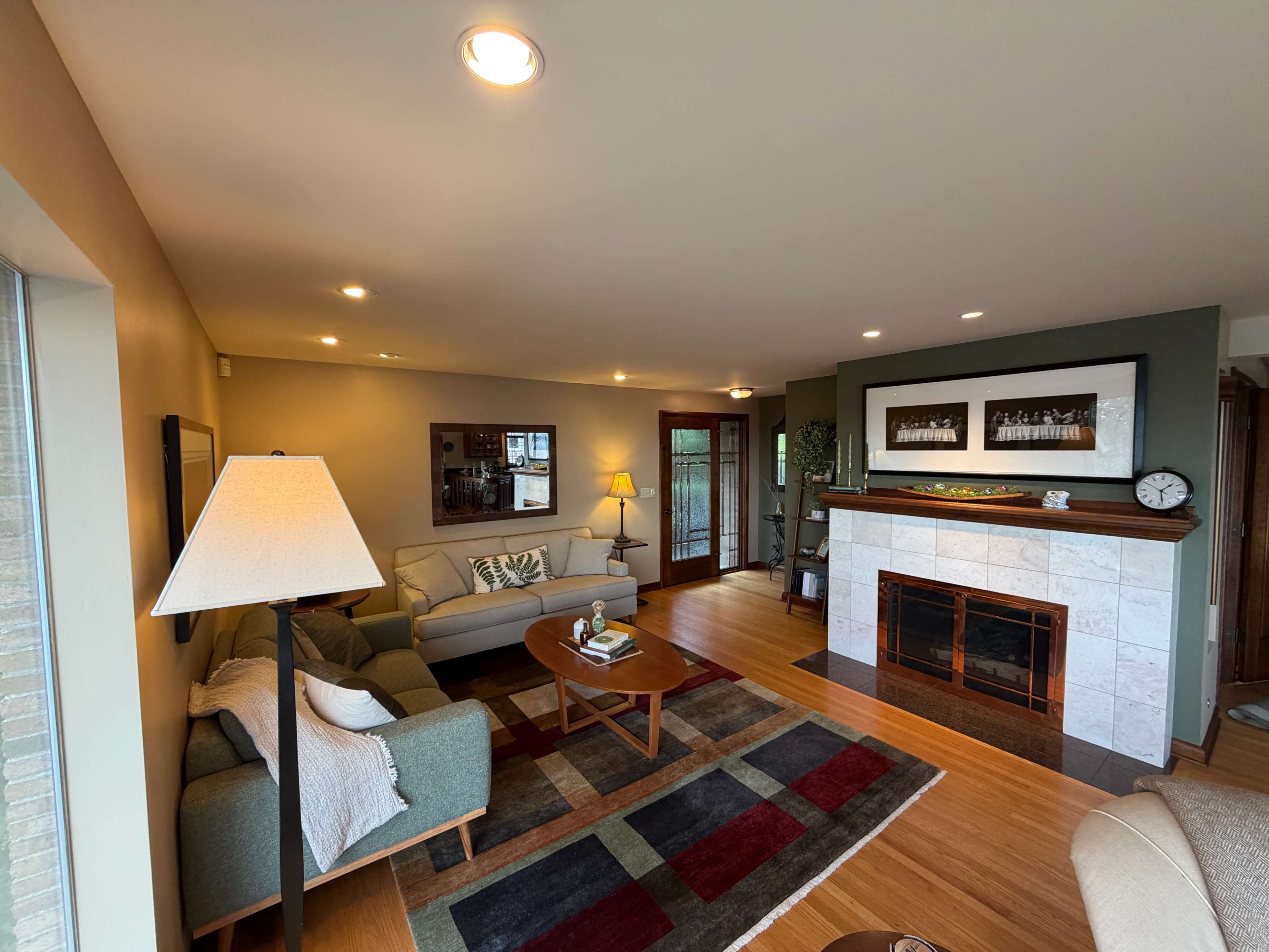 The image shows a living room with a fireplace, a couch, a coffee table, and large windows allowing natural light to enter.