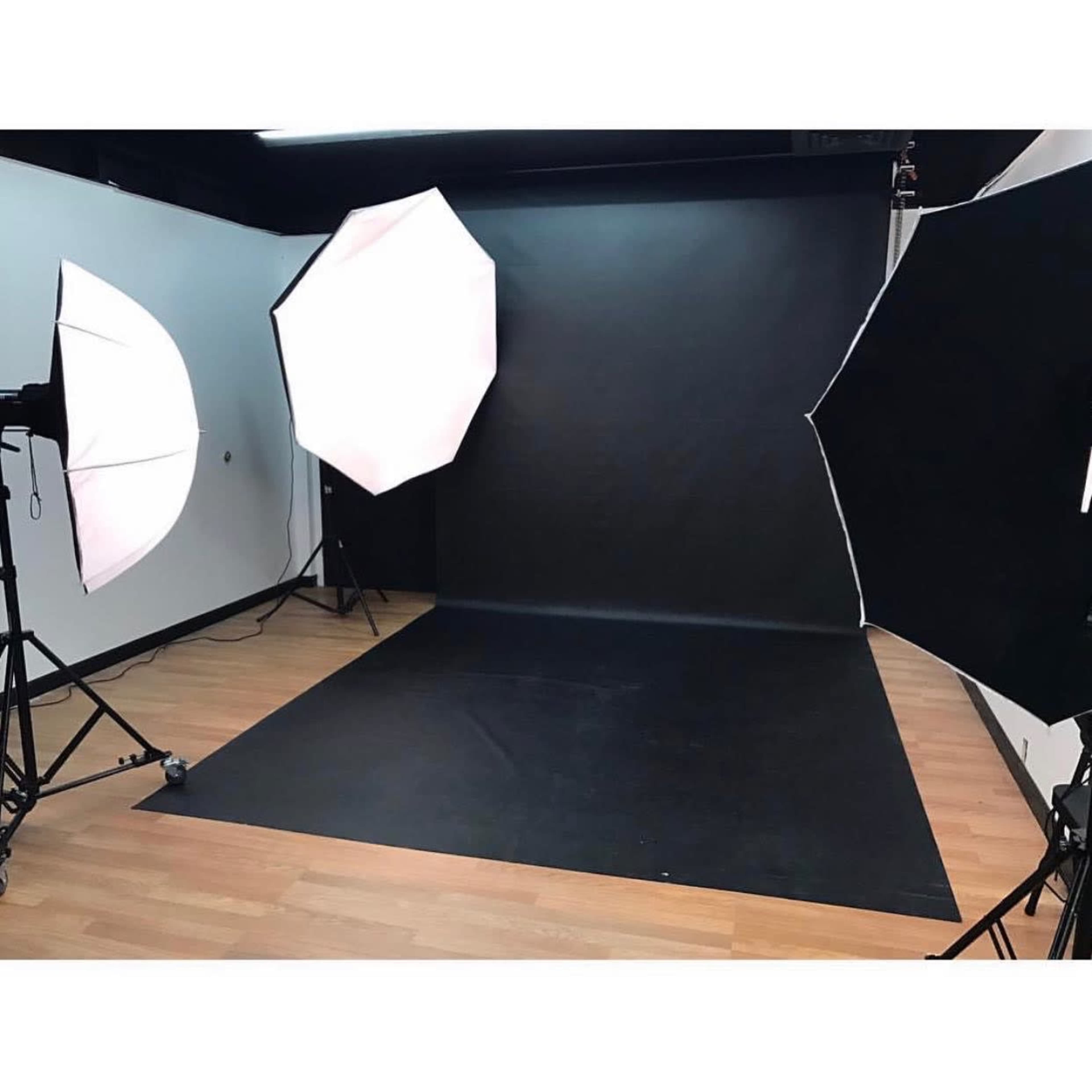 The image shows a photography studio setup with two softbox lights and a black backdrop on a wooden floor.