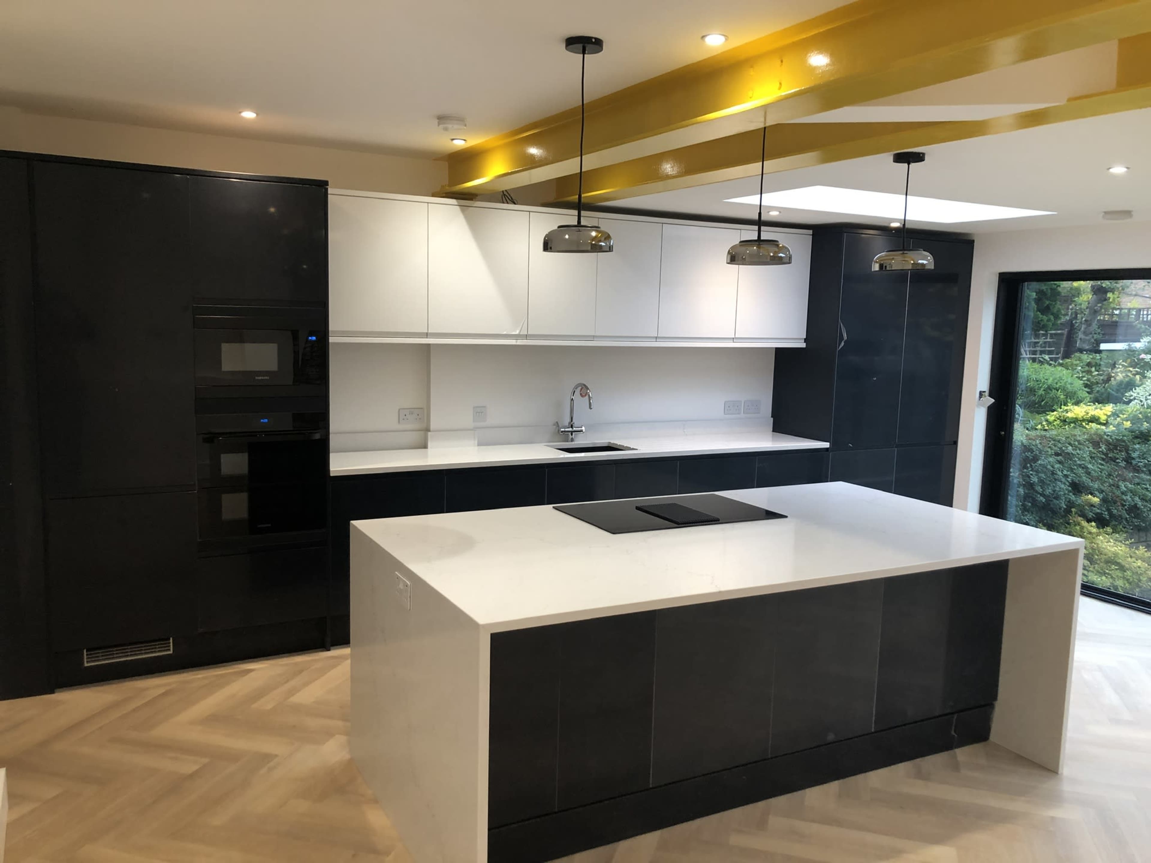 A modern kitchen features a central island with a white countertop, black and white cabinetry, and pendant lighting above.