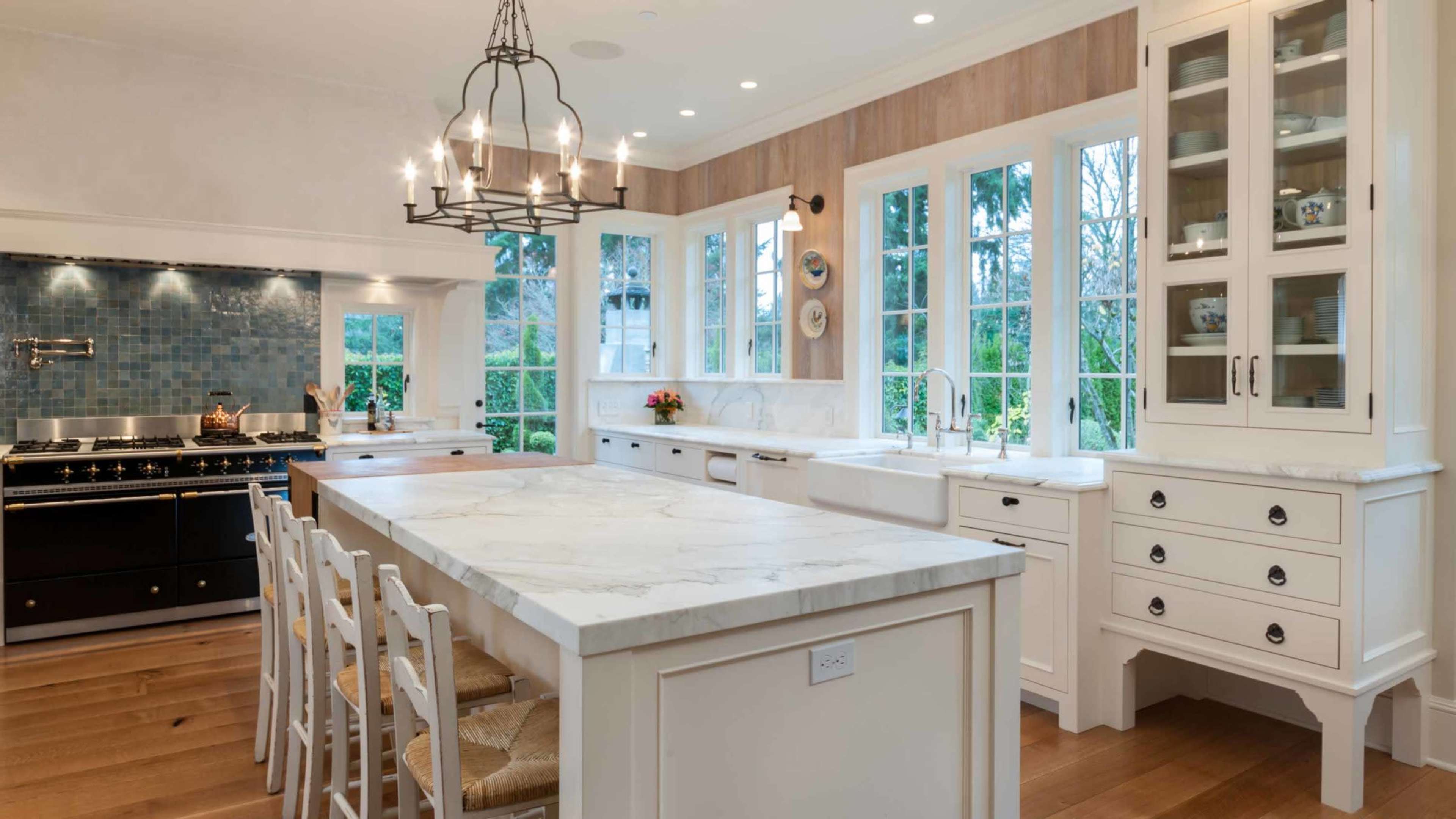 A modern kitchen with a large marble island, white cabinetry, and multiple windows that provide natural light.