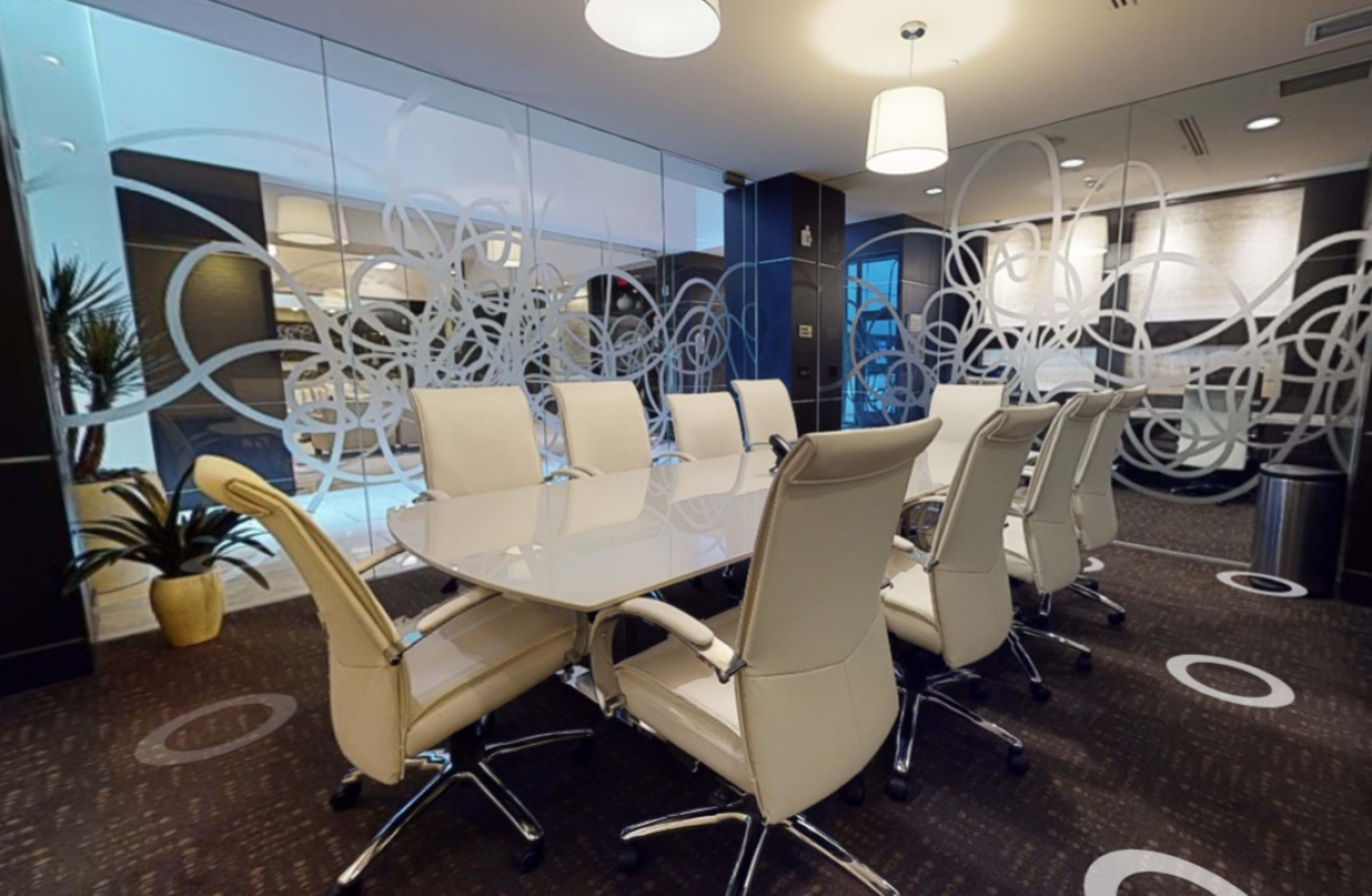 A conference room features a large, oval table surrounded by white leather chairs and is adorned with decorative glass panels.