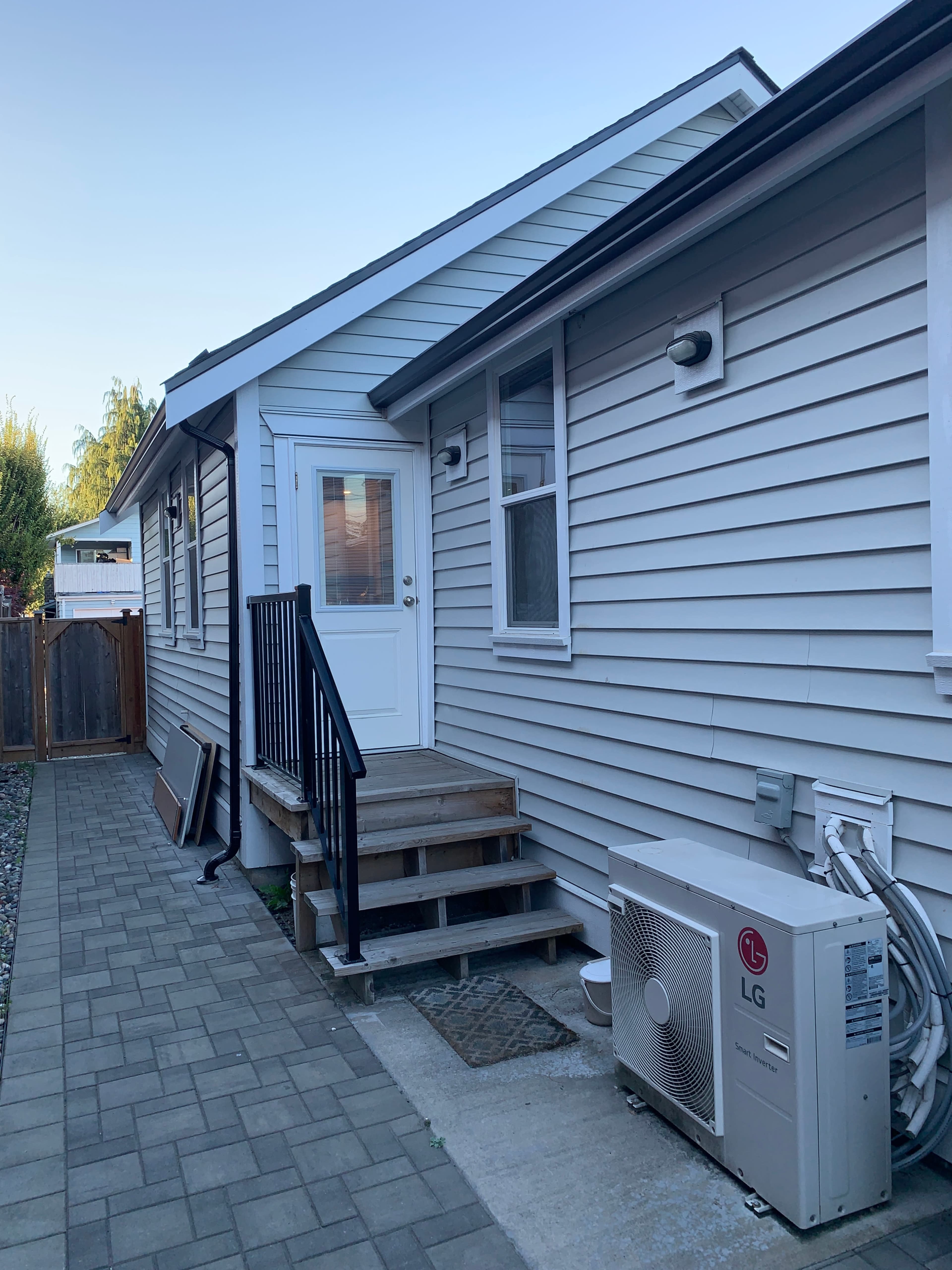 A gray house features a side entrance with stairs and an air conditioning unit beside it.