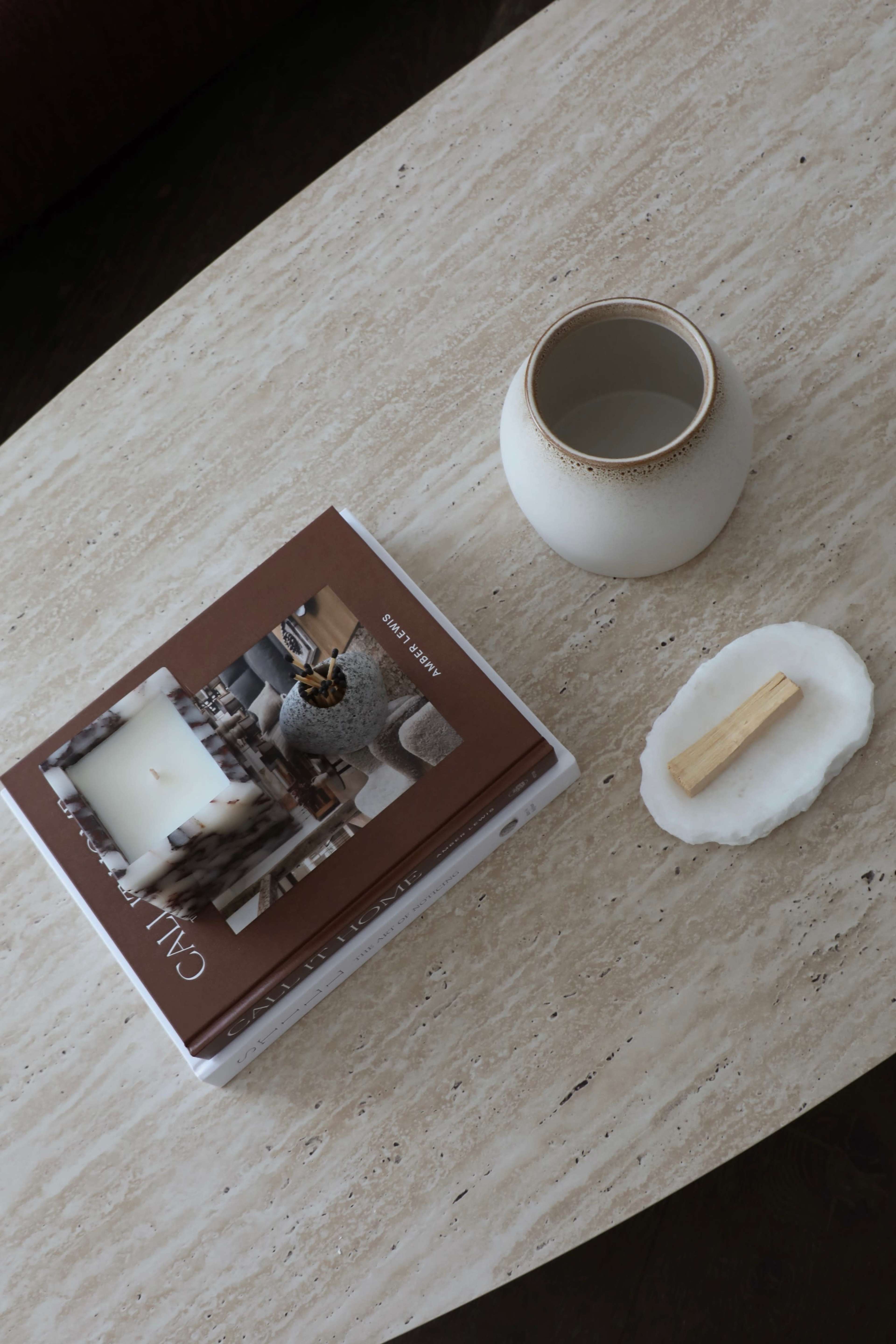 A marble table displays a book, a round ceramic vase, and a small white plate with a wooden stick on it.