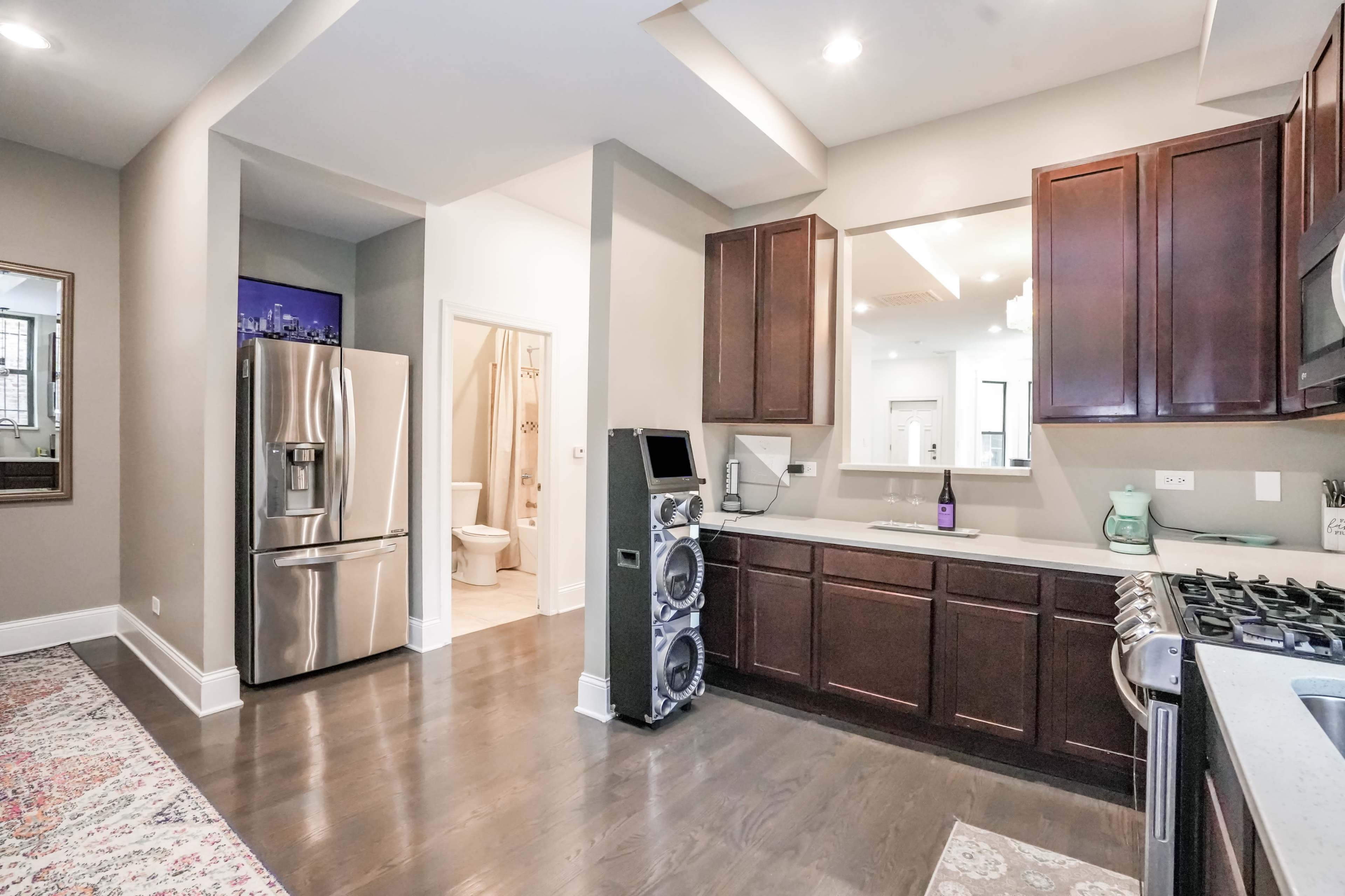 A modern kitchen with dark wooden cabinets, stainless steel appliances, and a small hallway leading to a bathroom.