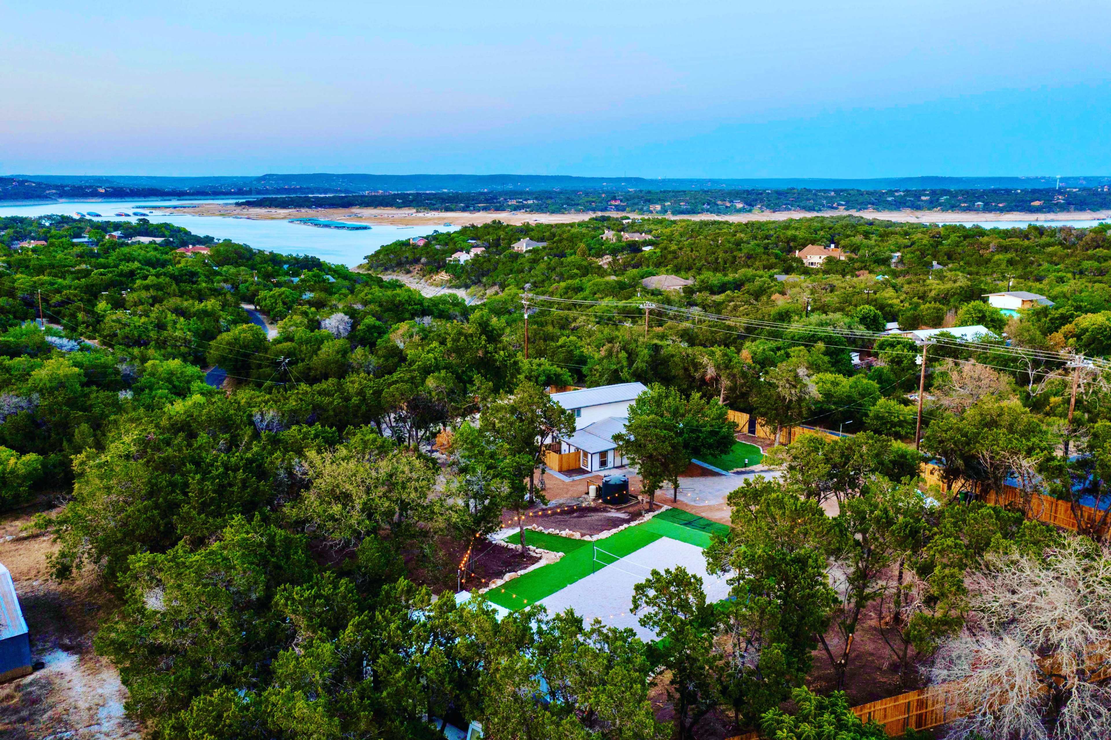 The image shows a bird's-eye view of a lush, green landscape featuring a house with a yard and a nearby body of water.