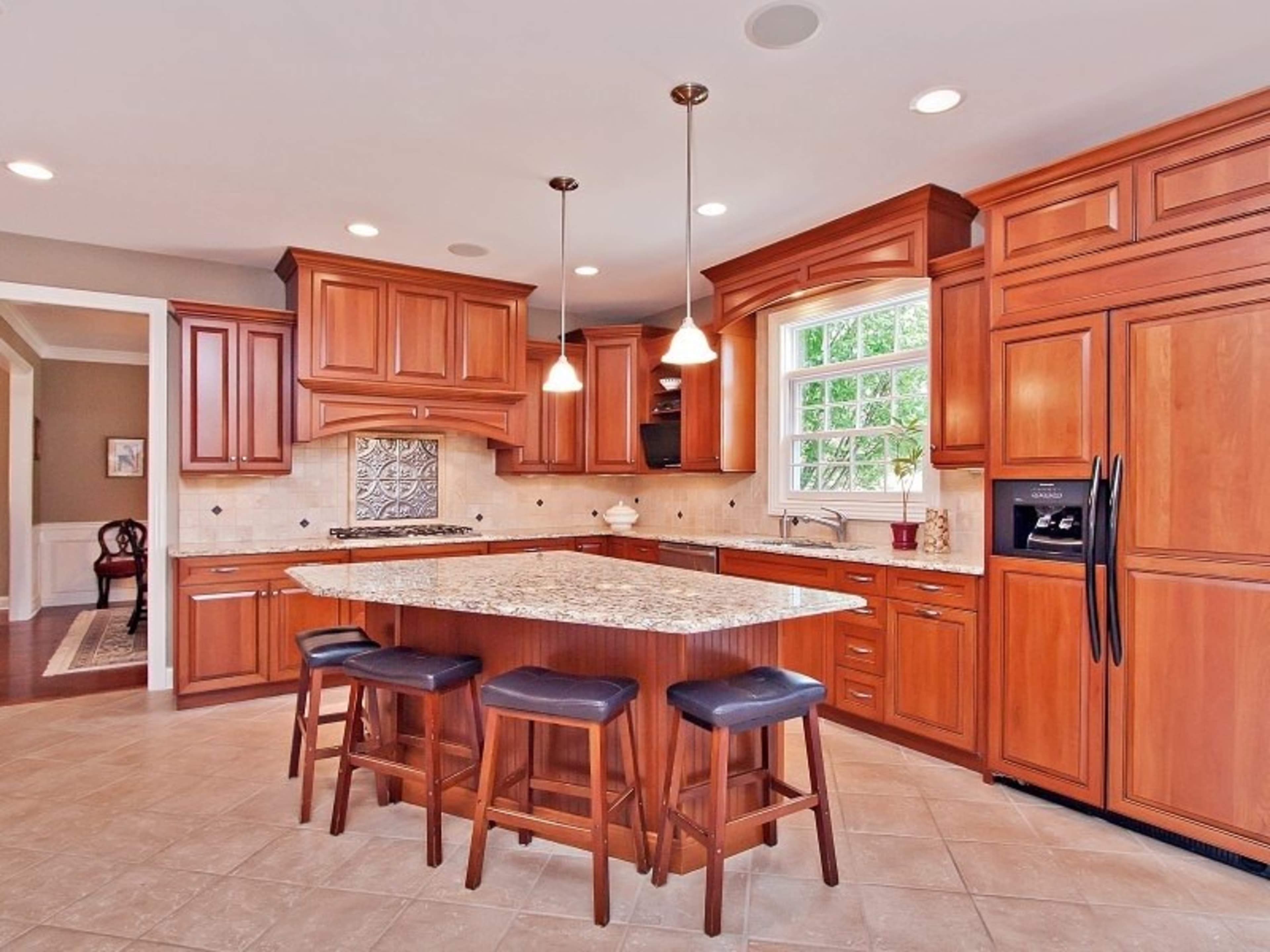 A modern kitchen with wooden cabinetry, a large island with a granite countertop, and pendant lighting above.