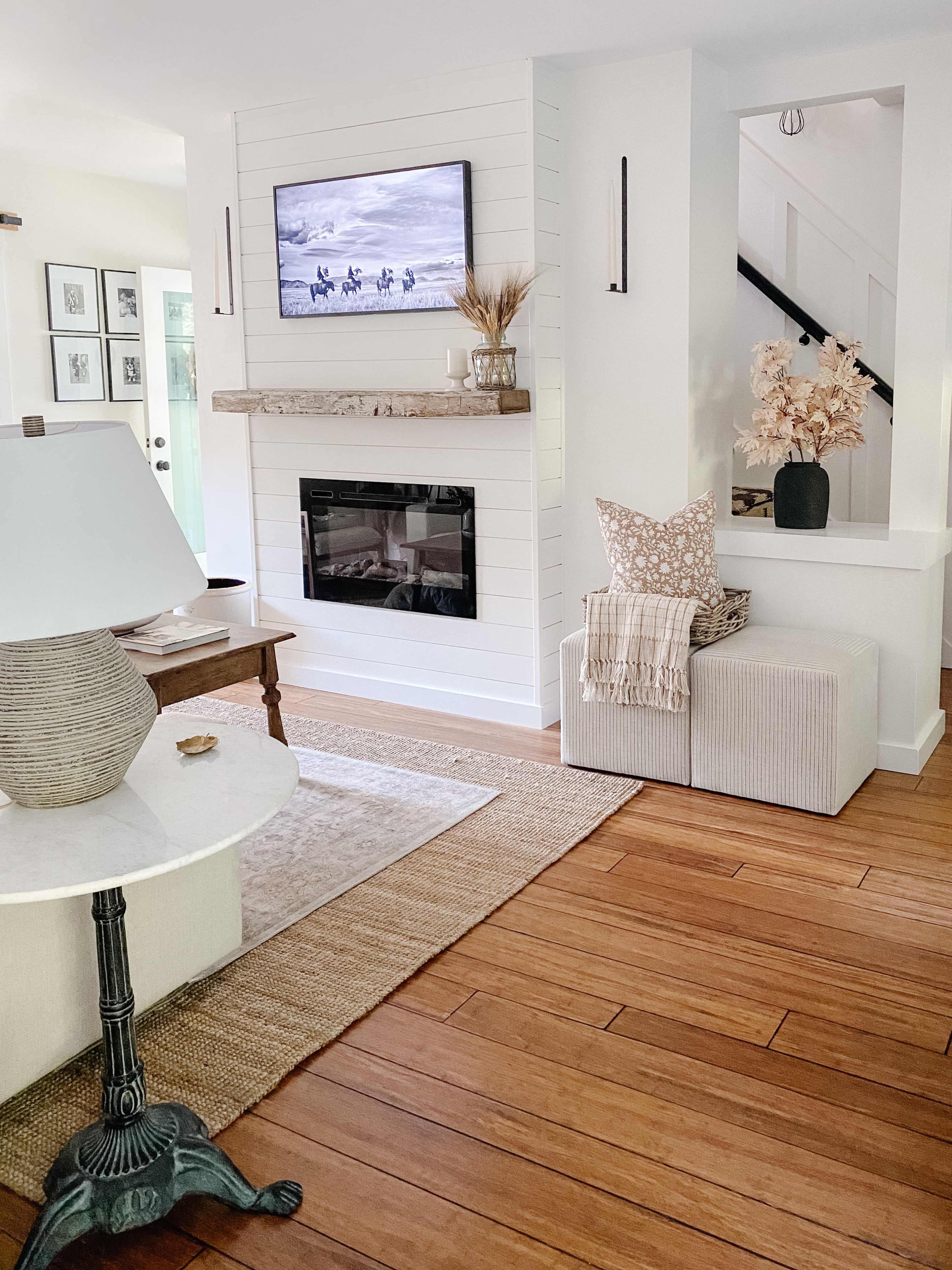A cozy living room features a mounted TV above a wooden mantel, a light-colored coffee table, and a sofa with decorative pillows.