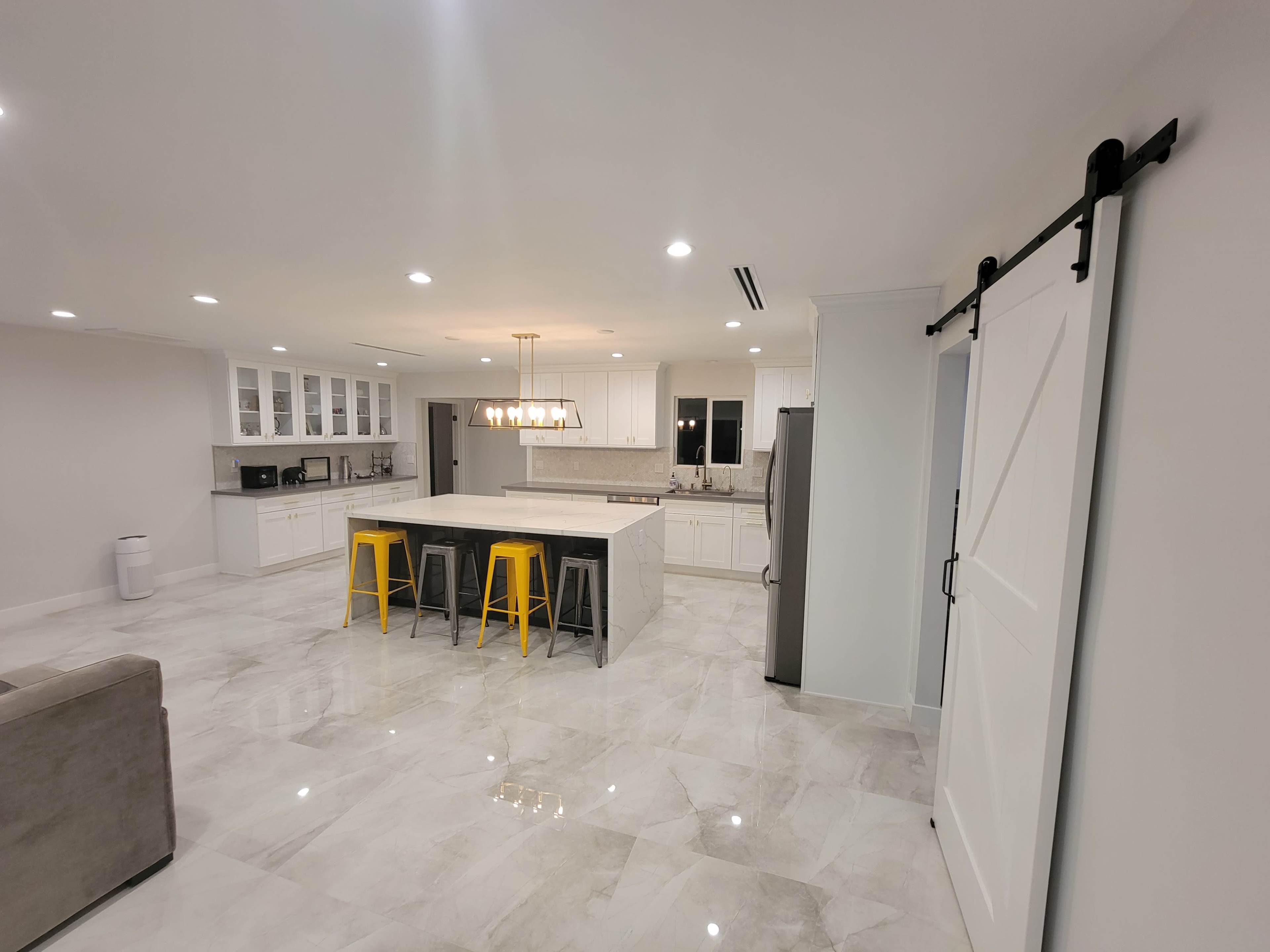 A modern kitchen with white cabinets, a large island with three stools, and a sliding barn door.