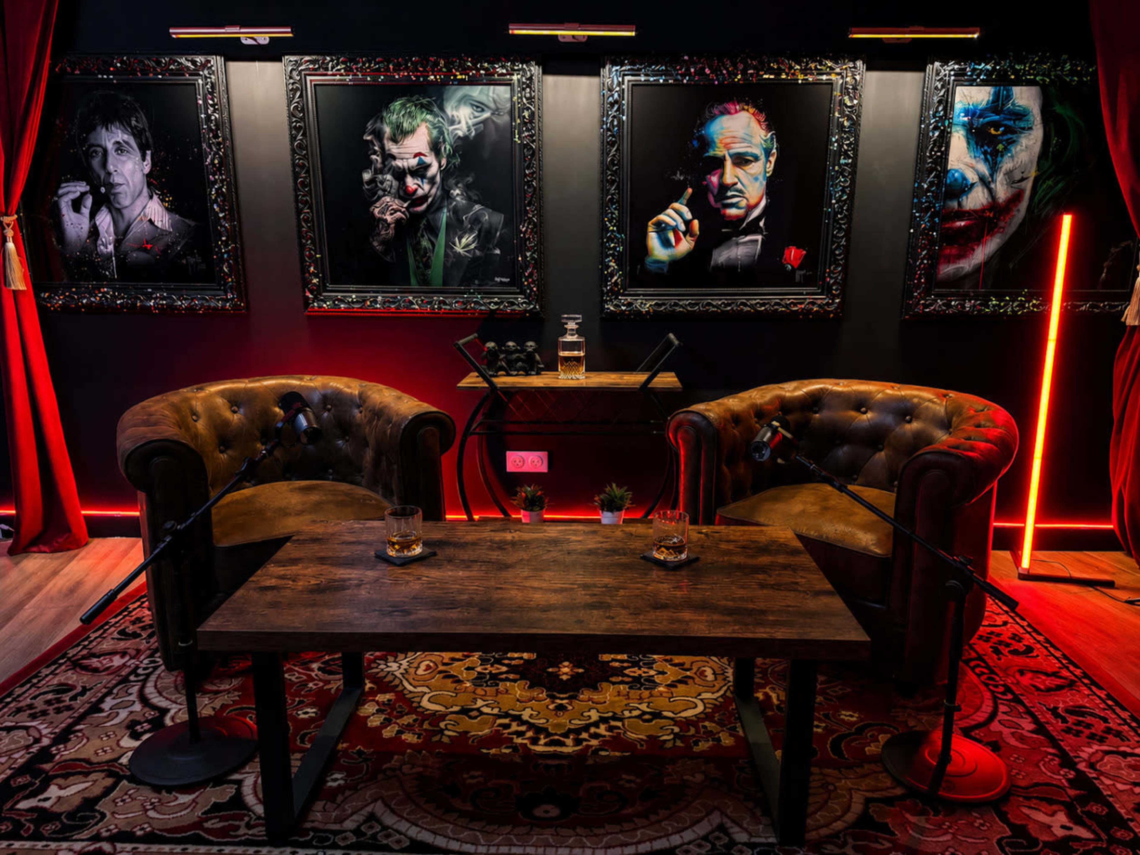 The image shows a cozy lounge area featuring two tufted leather chairs, a wooden table, and four dramatic framed portraits of iconic characters on a dark wall.