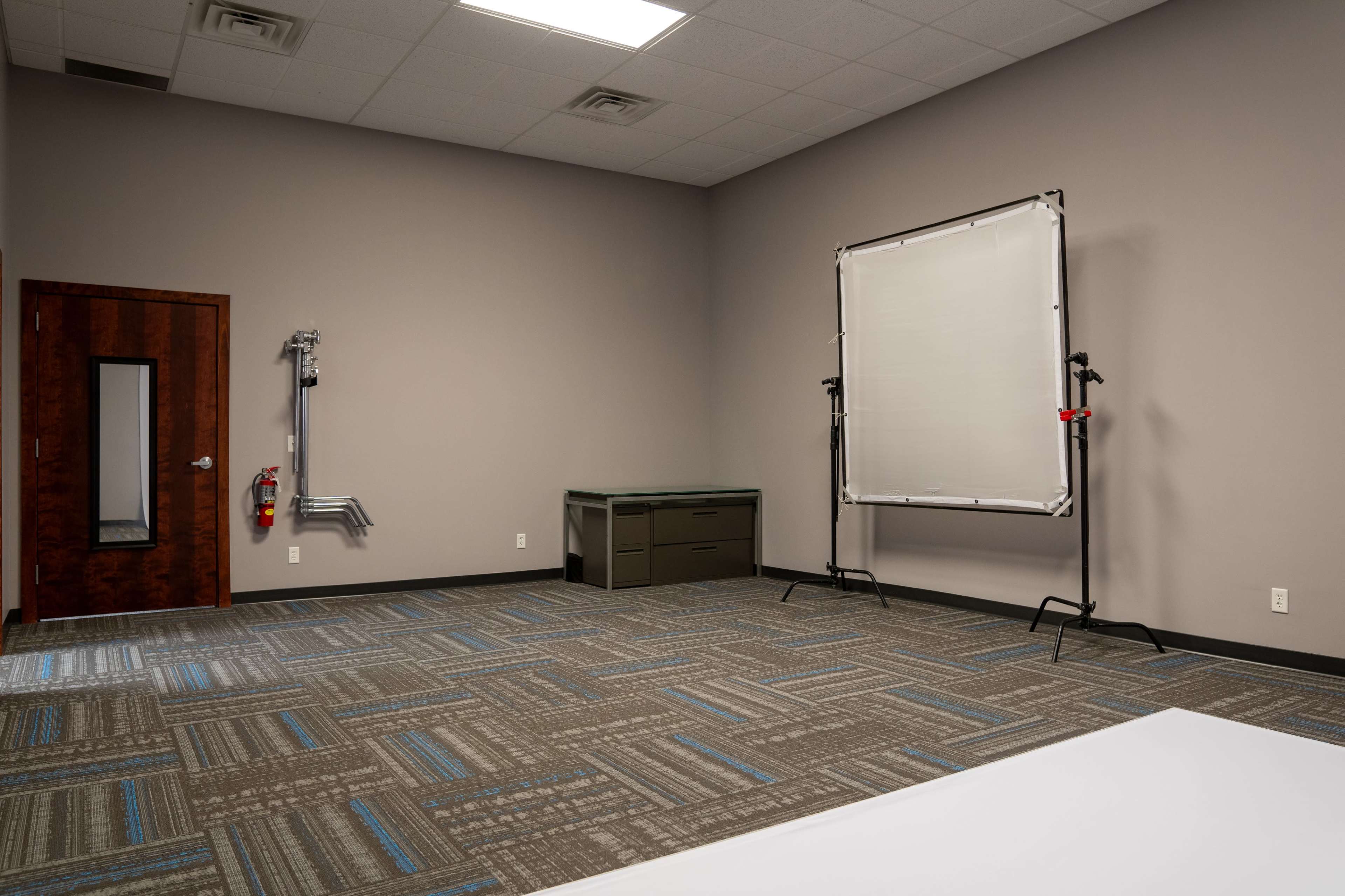 The image shows an empty room with gray walls, a door on the left, and a backdrop frame positioned to the right.