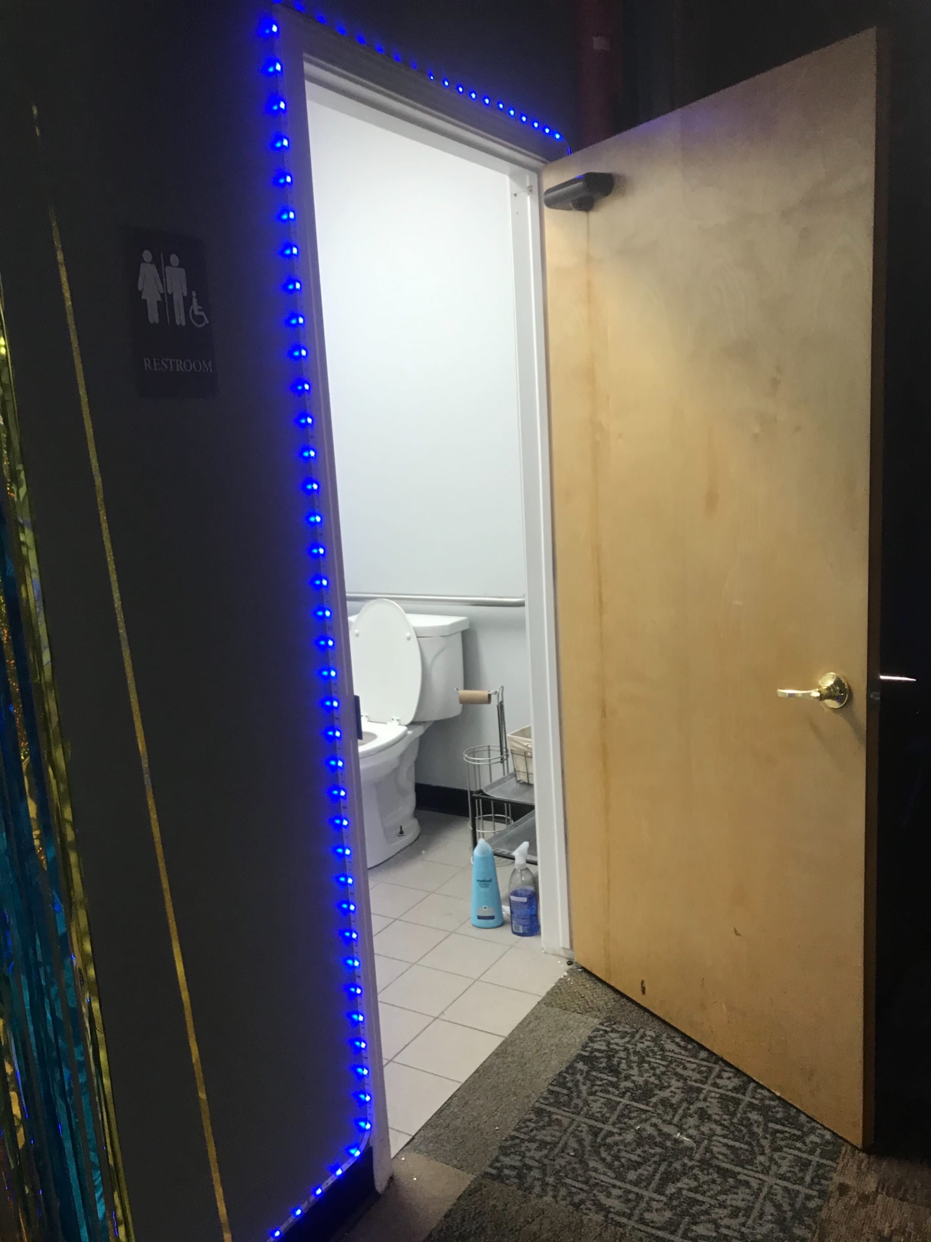 A bathroom door with blue LED lights around the frame stands ajar, revealing a toilet inside.