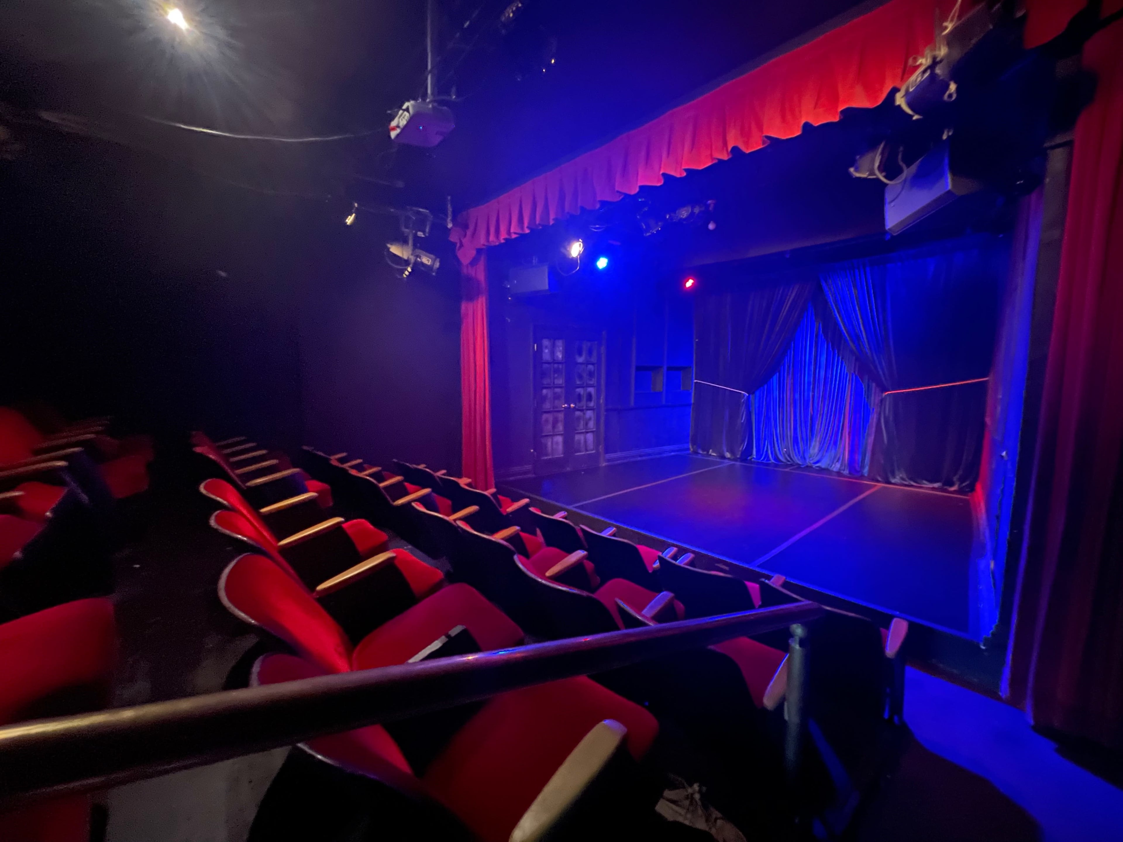 A small theater with red seating facing a stage illuminated by blue and purple lights.