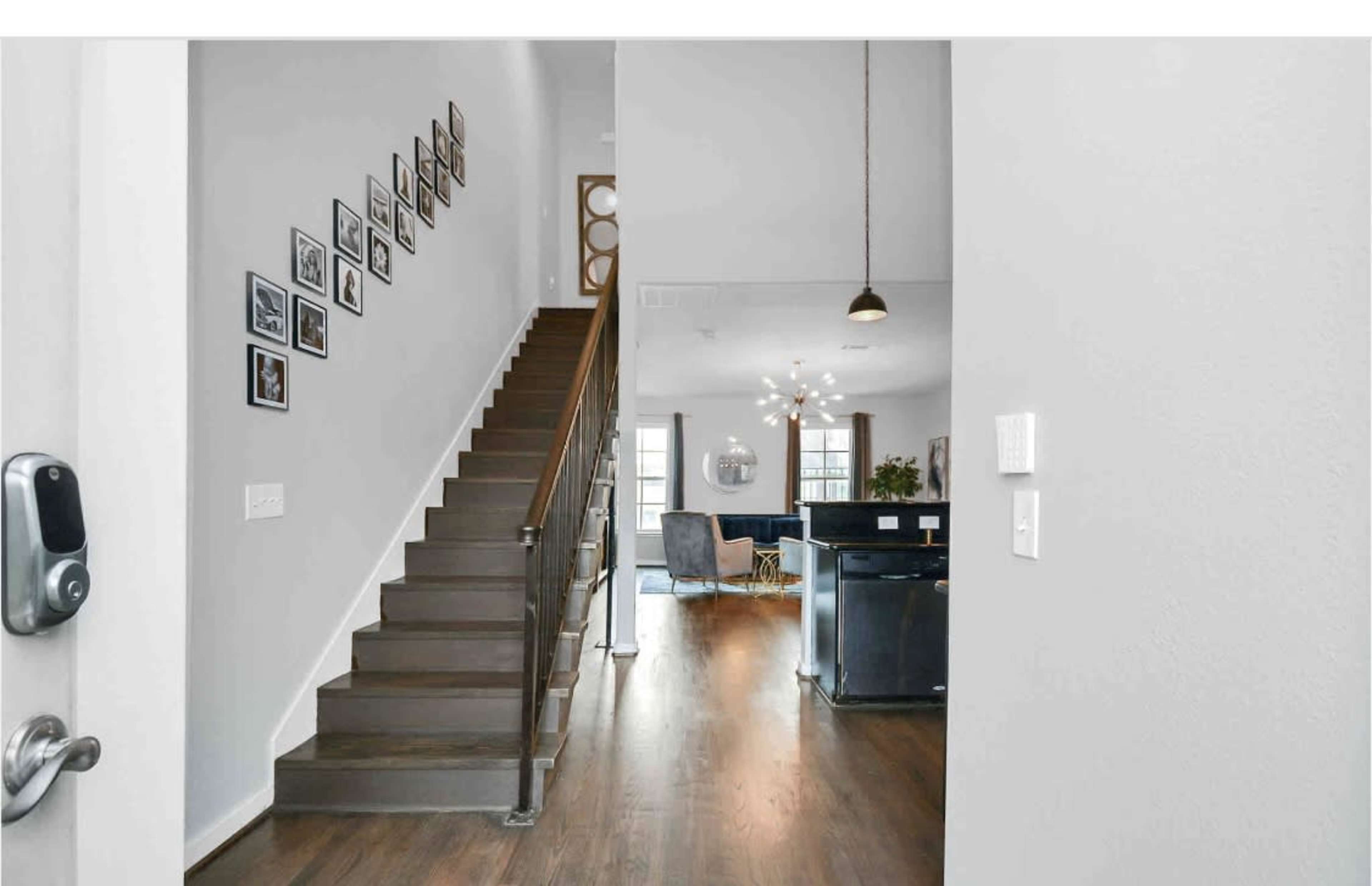 A staircase with framed photos is visible in a hallway that leads to an open living area with modern furniture.