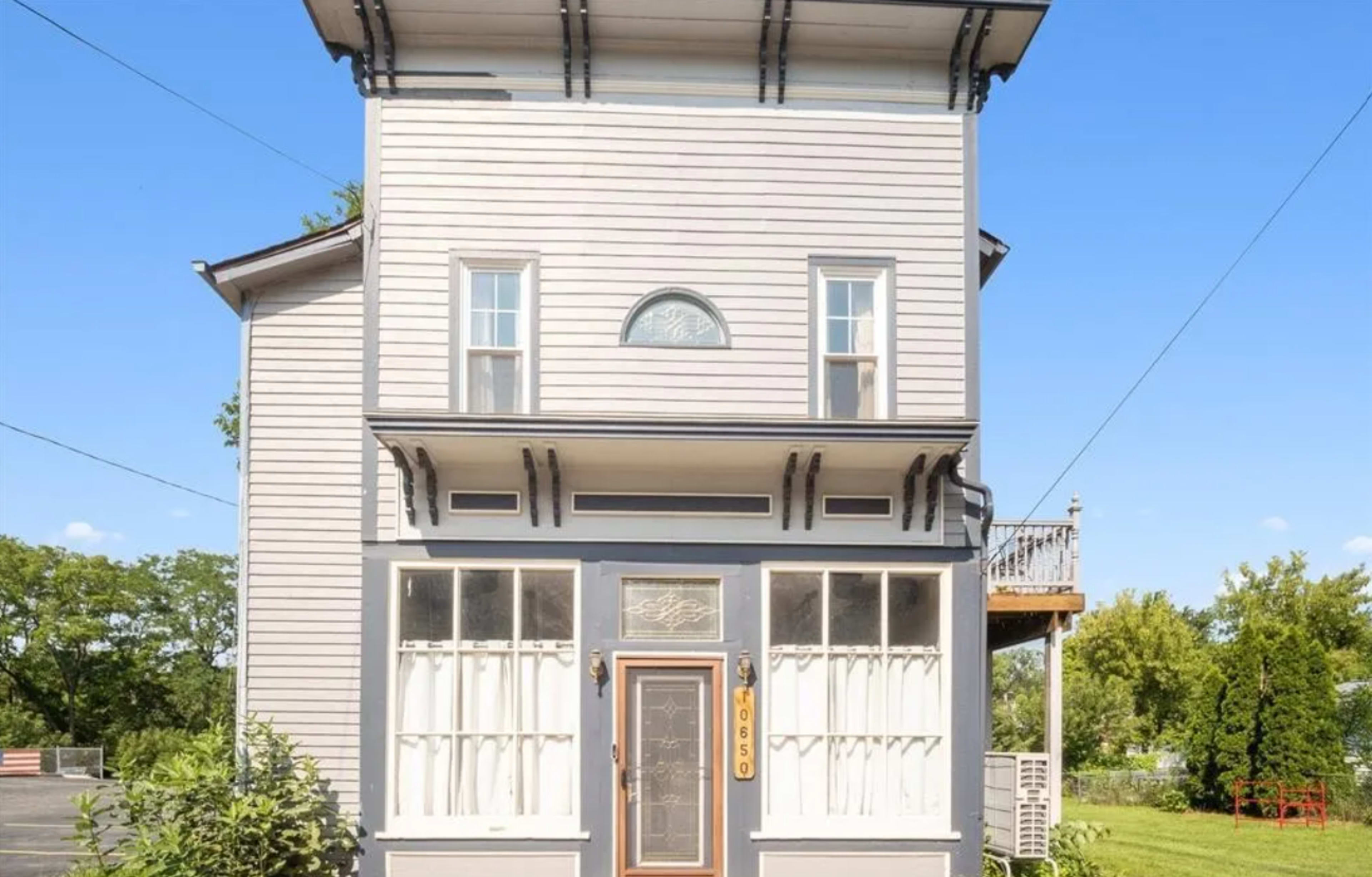 The image shows a three-story, light-colored house with large front windows and a decorative entrance door.
