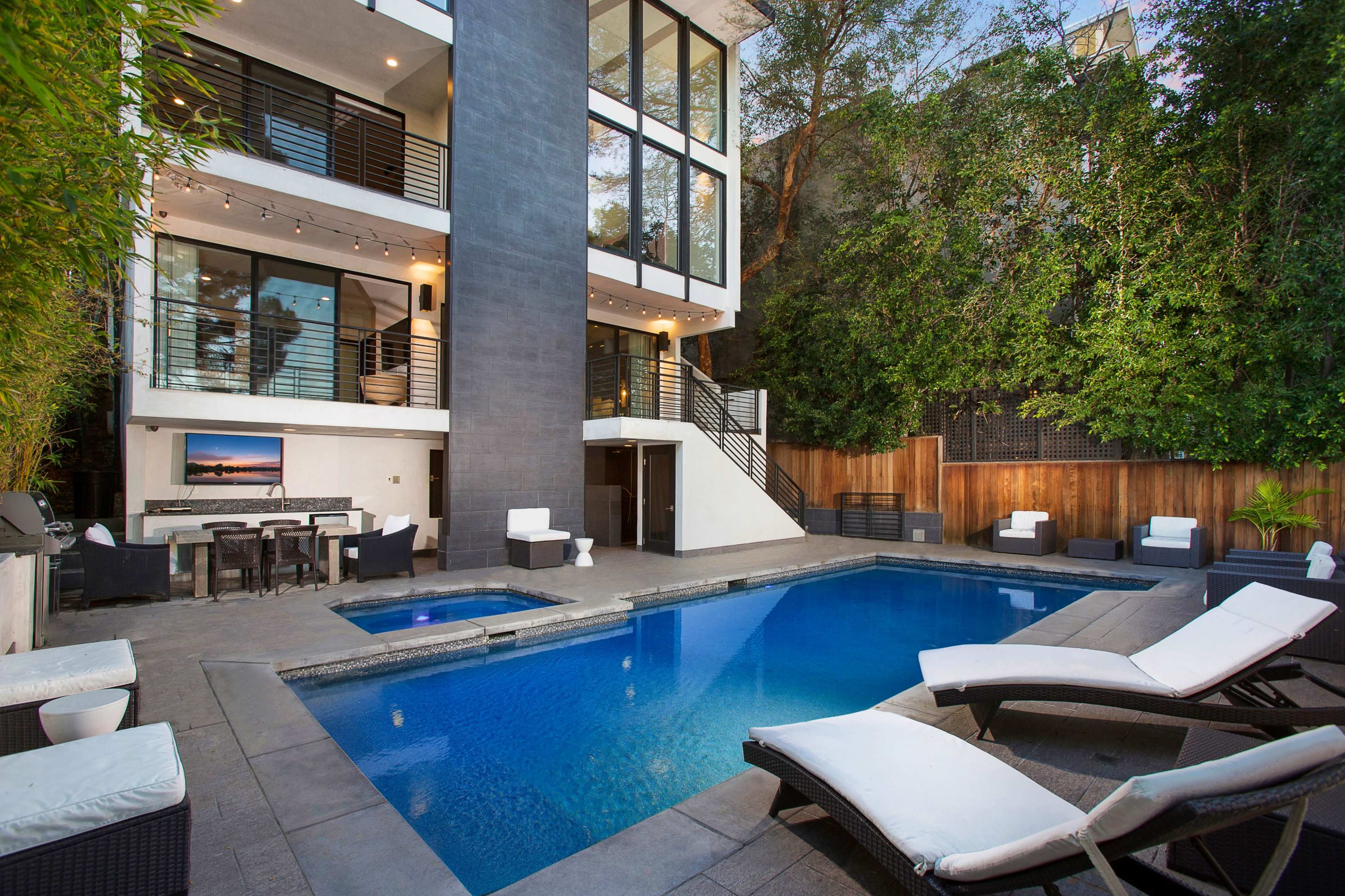 A modern home with large glass windows overlooking a swimming pool and outdoor seating area.