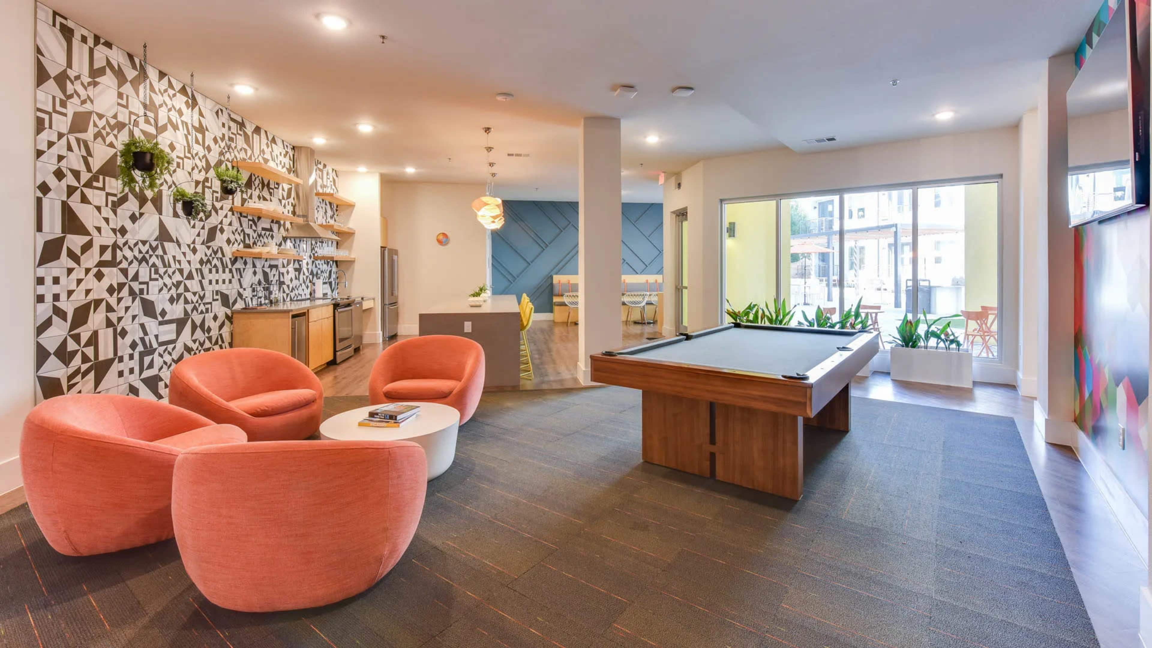 The image shows a modern lounge area featuring pink chairs, a pool table, and a wall with geometric patterns.