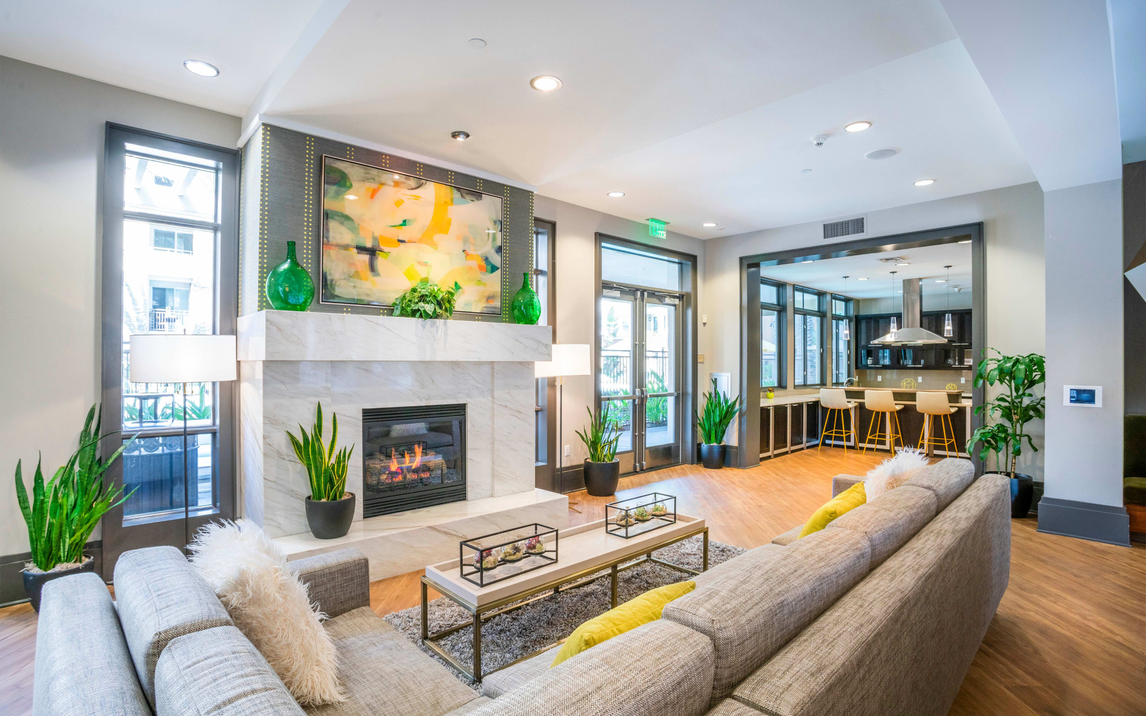A modern living room with a fireplace, large windows, a gray sectional sofa, and a bar area in the background.