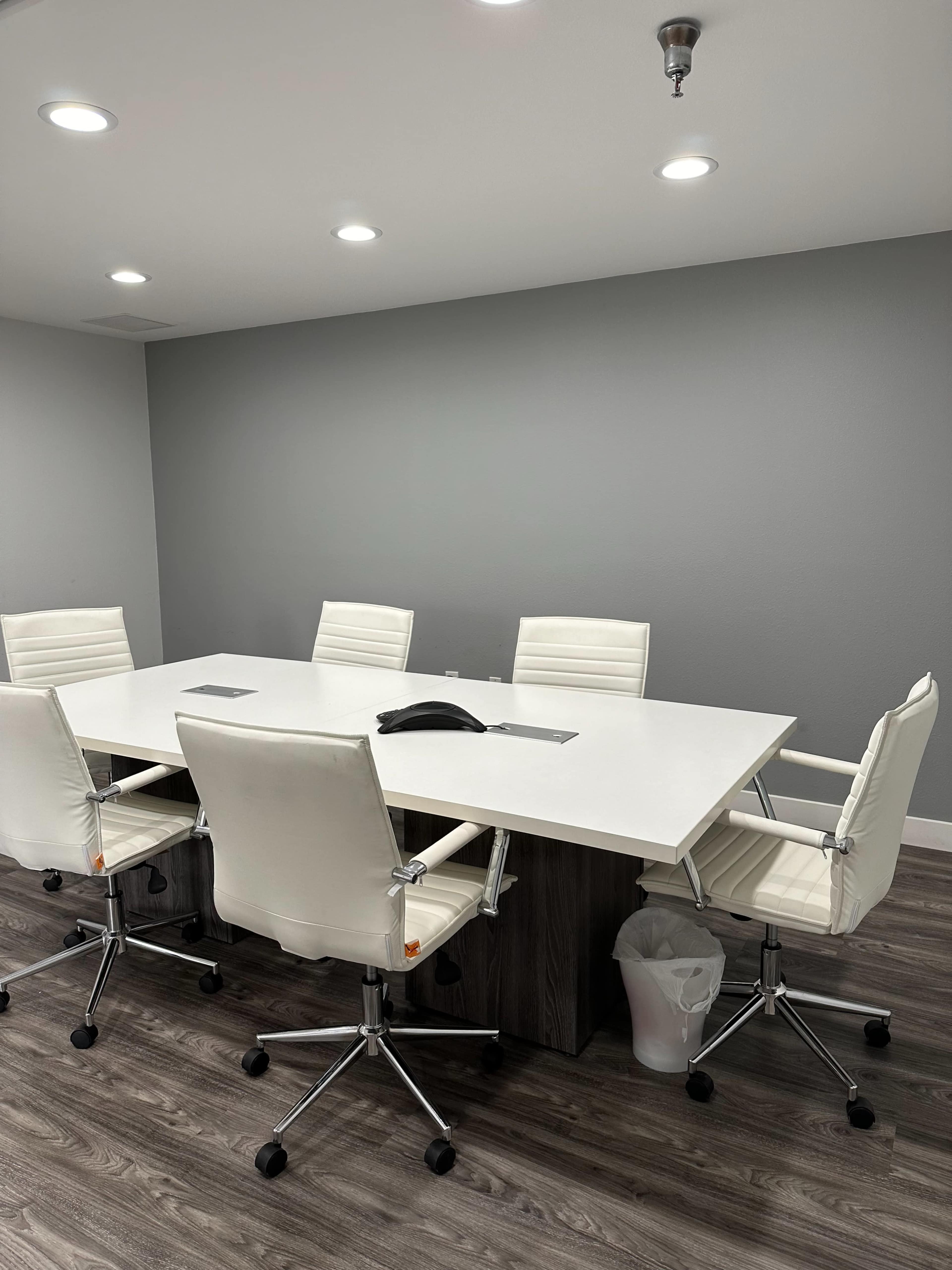 The image shows a modern conference room with a large white table surrounded by six white ergonomic chairs.