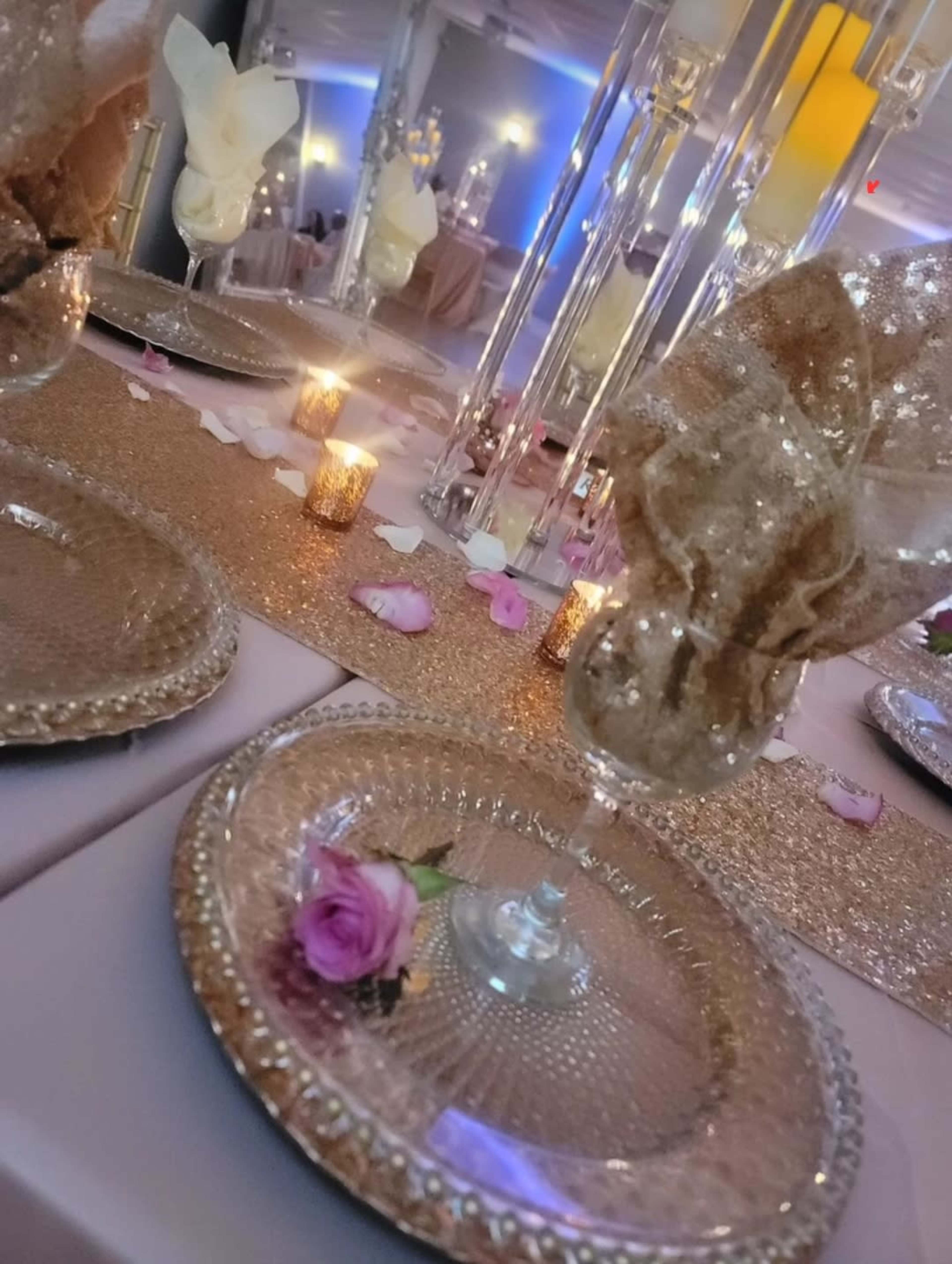 The image shows a beautifully set dining table decorated with sparkling plates, elegant napkin folds, candles, and rose petals.