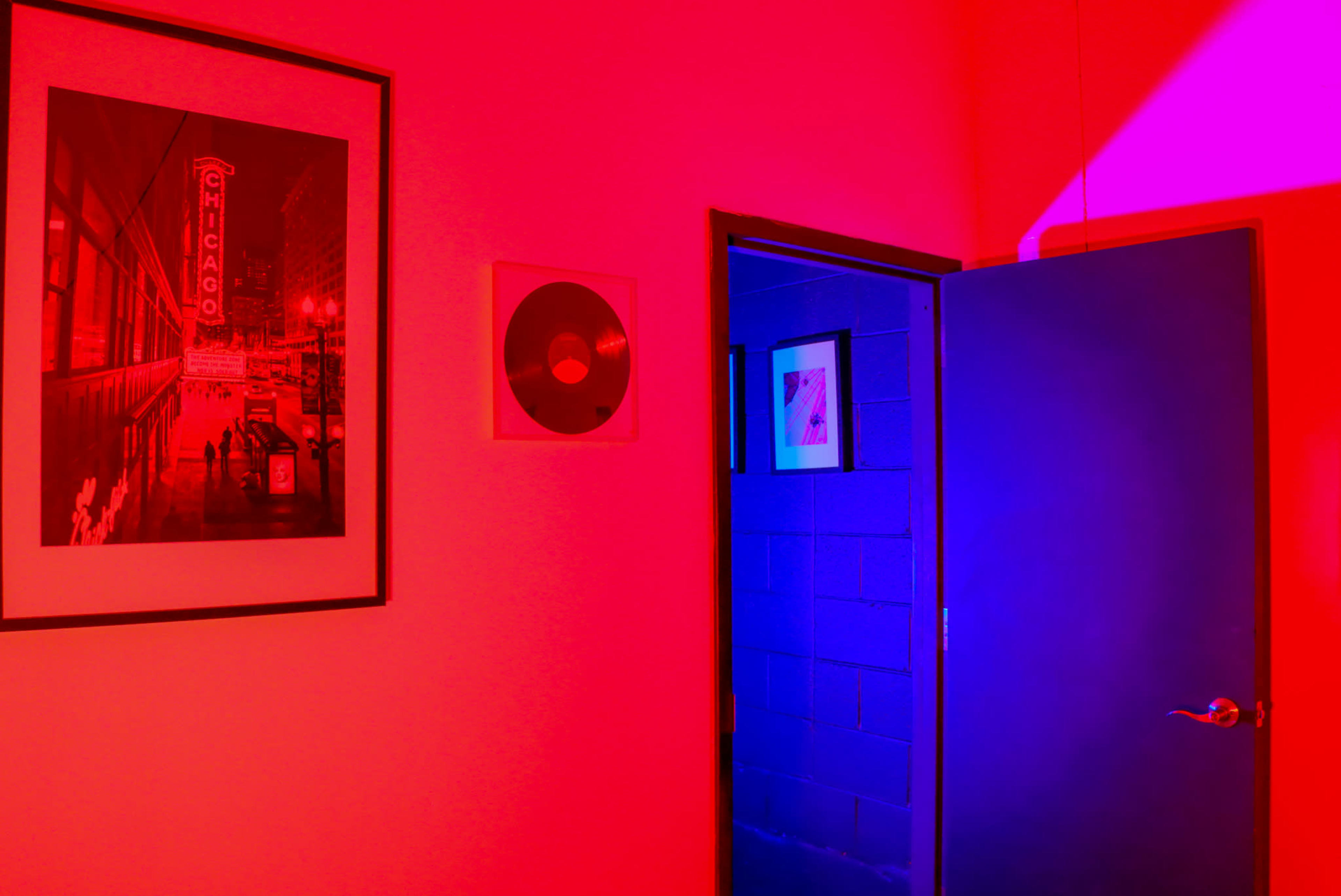 A red-lit room features a framed photograph of Chicago on the wall and a partially open blue door leading to a darker space.