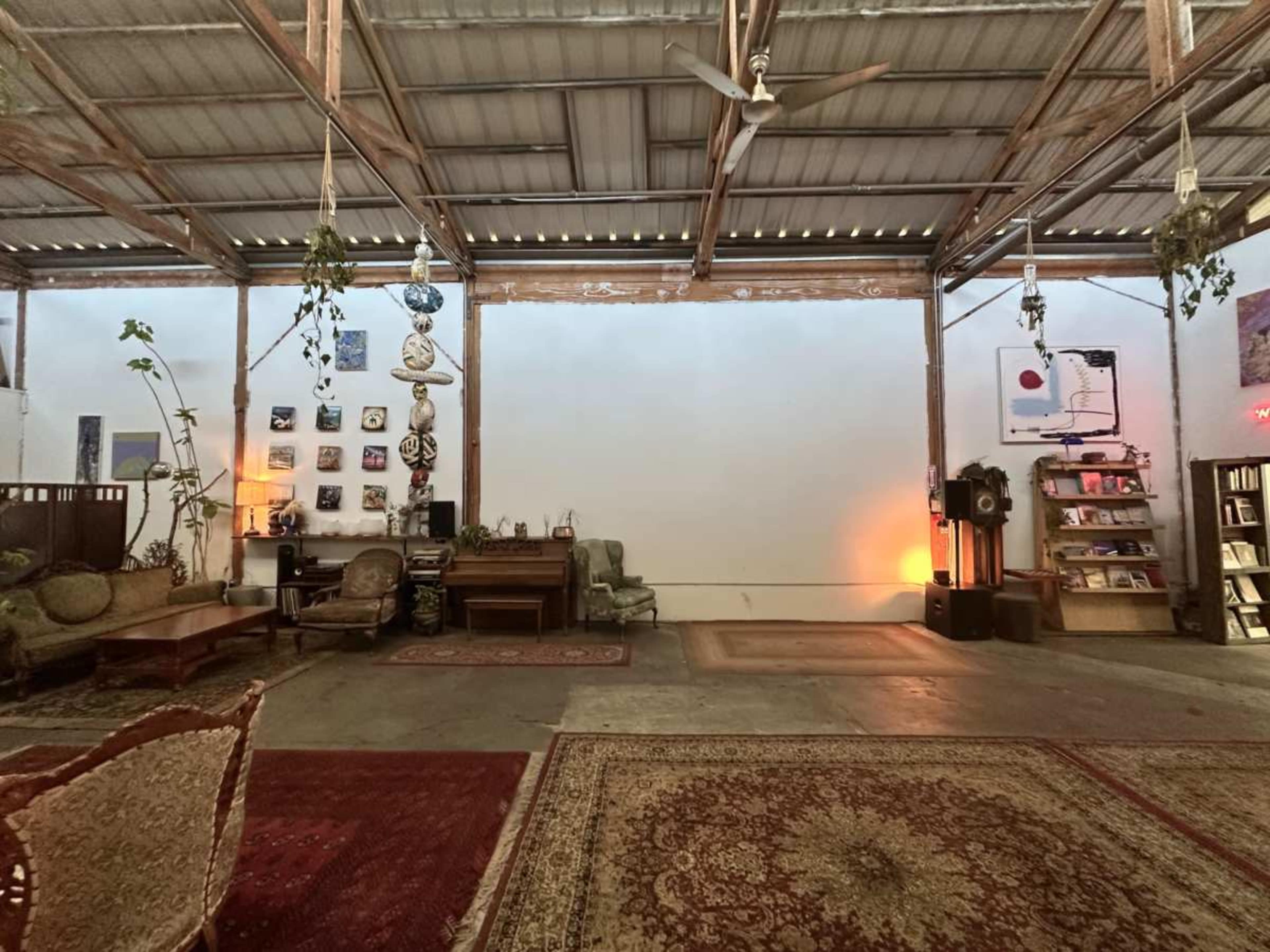 The image shows an open, spacious interior with various seating areas, decorative rugs, and wall art under a metal roof.