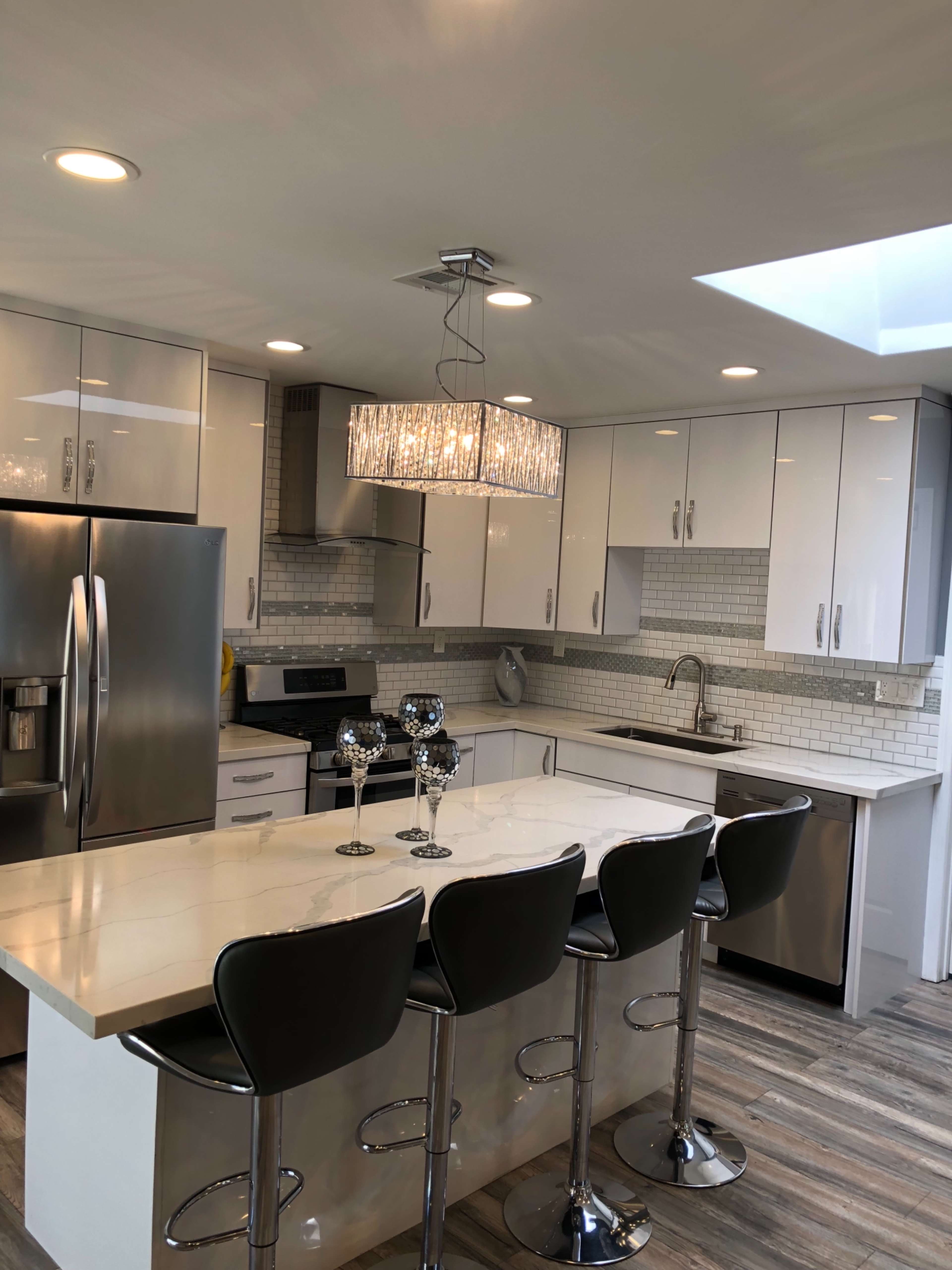 A modern kitchen with stainless steel appliances, white cabinetry, and a large island with four black barstools.