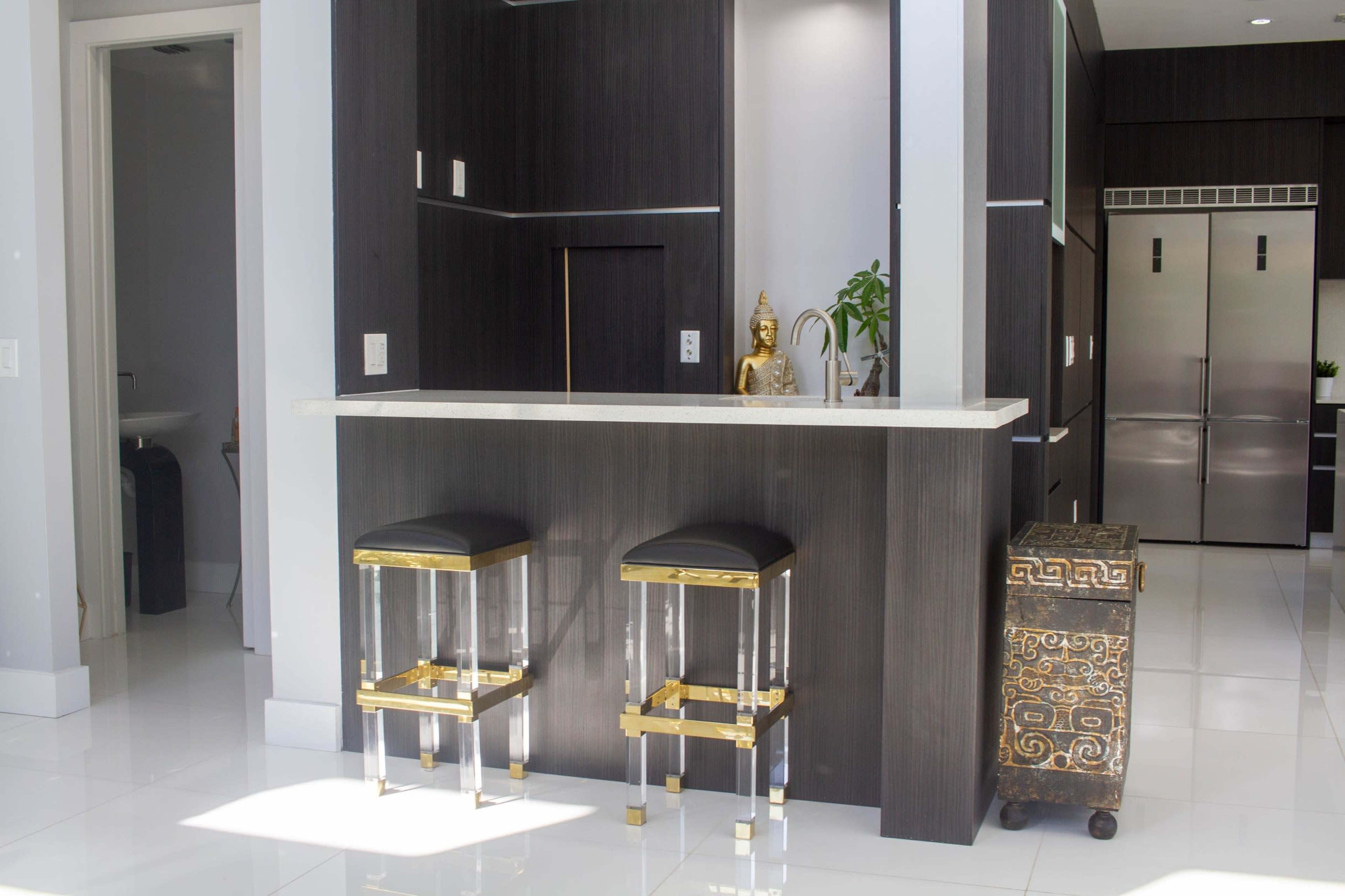 A modern kitchen features a sleek bar area with two black stools and a decorative cabinet.