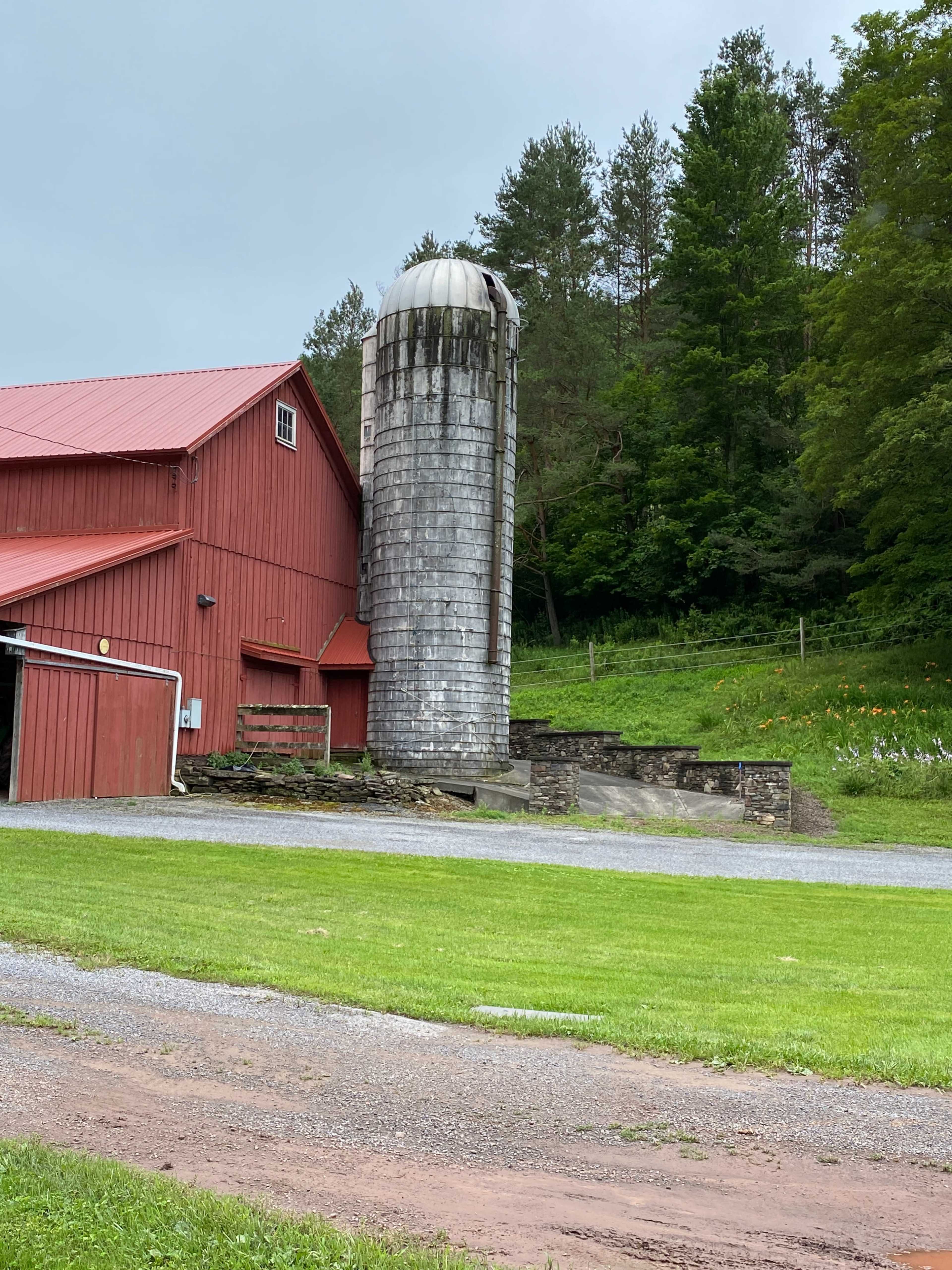 A red barn alongside a wooden silo, with a green grassy area and trees in the background.