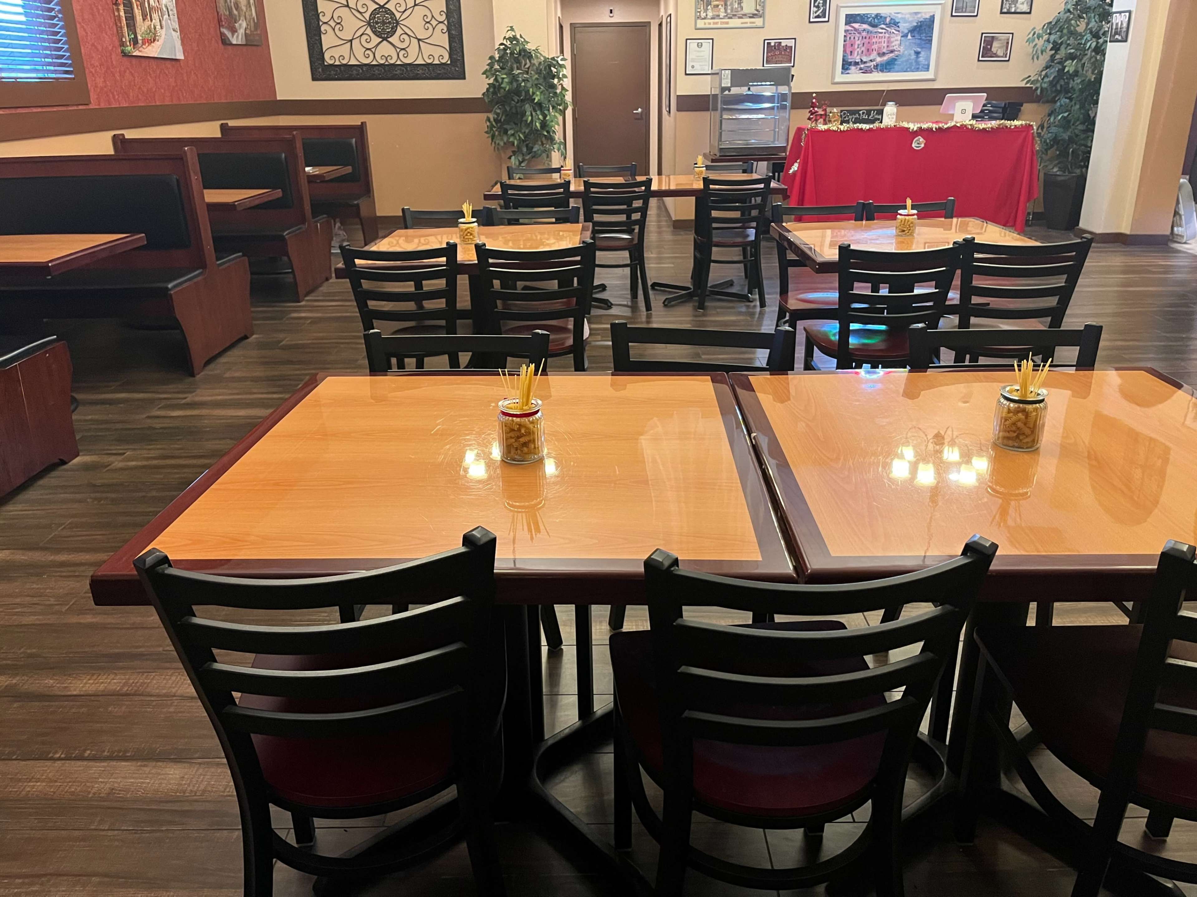 A restaurant interior with wooden dining tables and black chairs arranged neatly in a seating area, featuring booth seating along the walls.