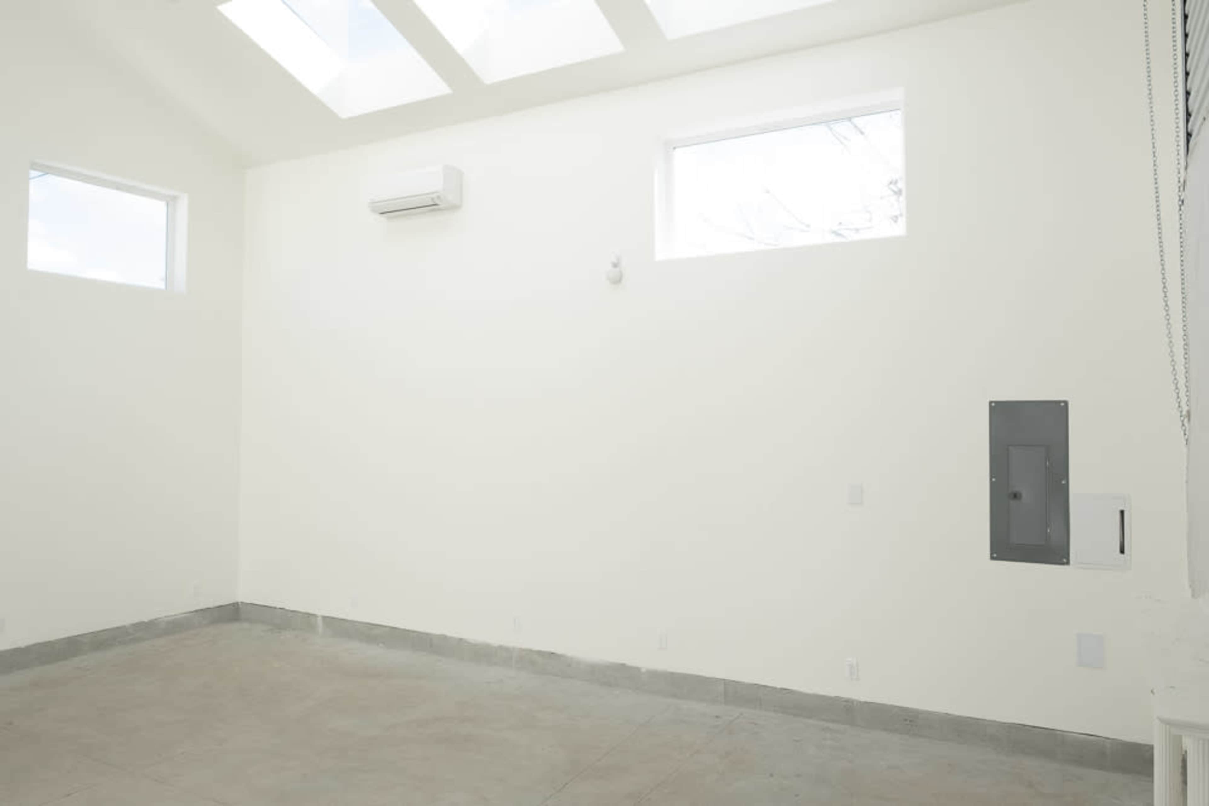 The image shows an empty room with white walls, a concrete floor, and windows along the top.