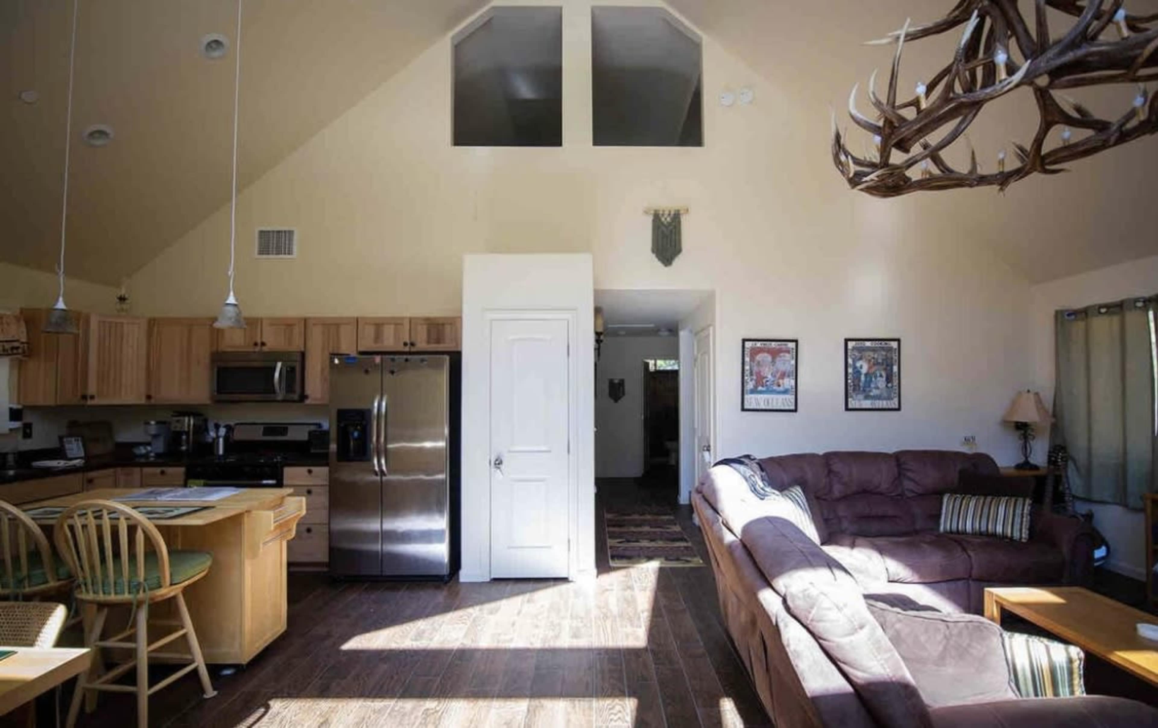 The interior of a spacious, well-lit cabin with a kitchen area, a living room featuring a large sofa, and high ceilings.