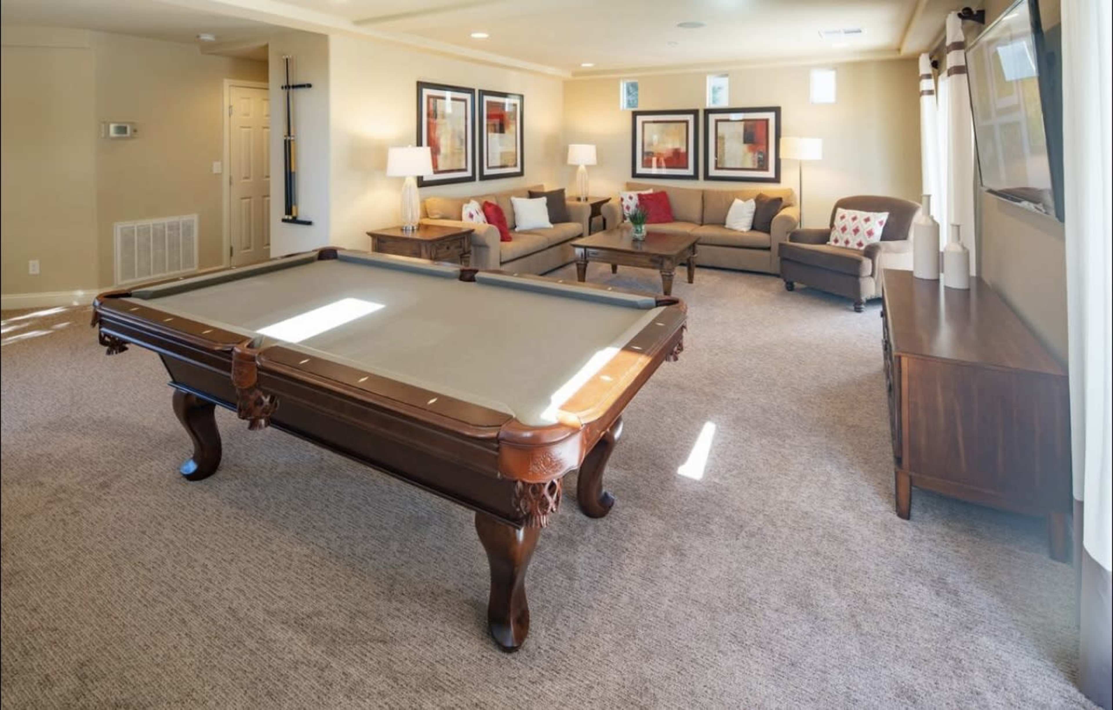 The room features a pool table in the center, surrounded by sofas and lamps, with modern artwork on the walls.