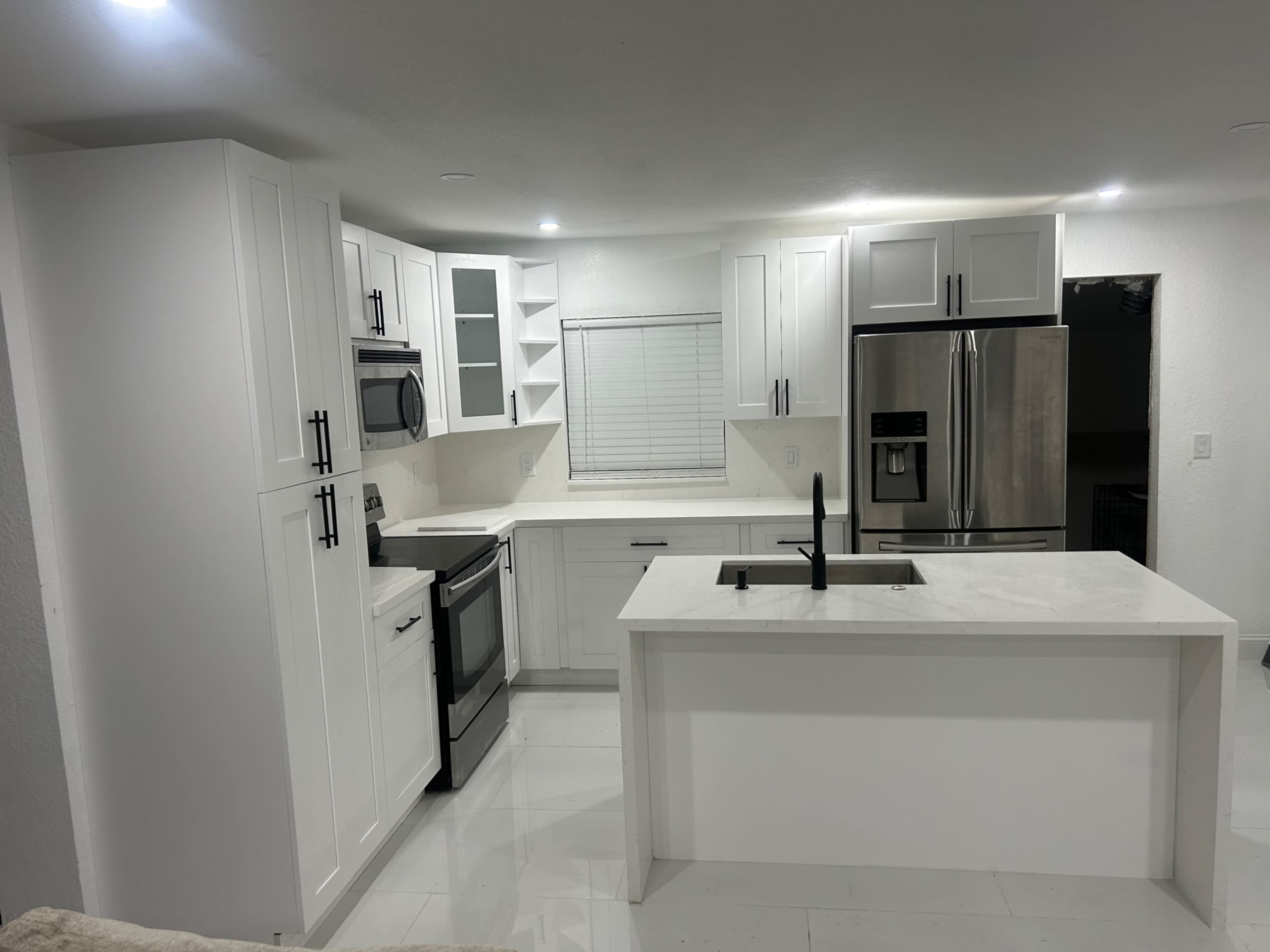 The image shows a modern kitchen with white cabinetry, stainless steel appliances, and a central island with a sink.