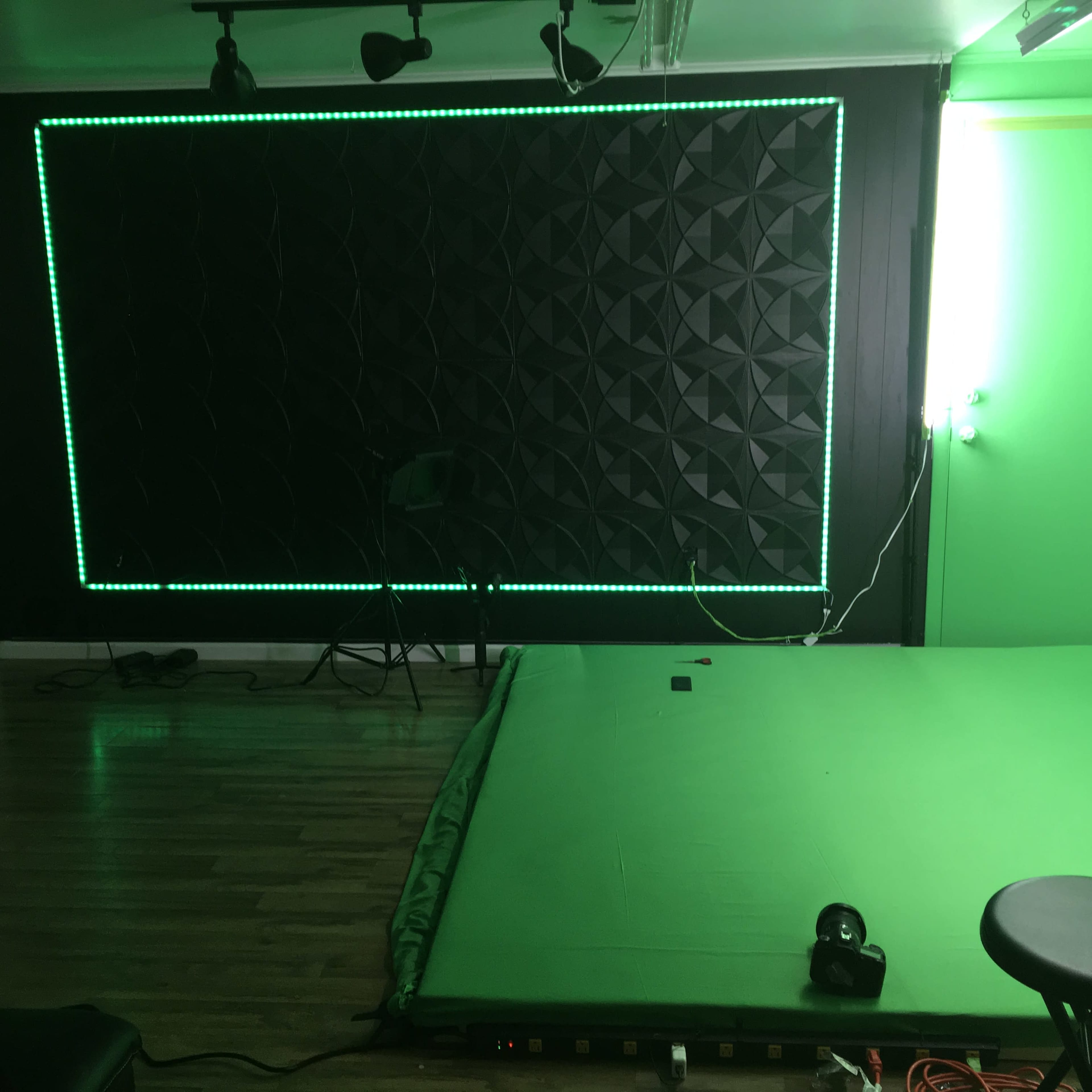 A room with a green backdrop and textured black wall, illuminated by green LED lights.