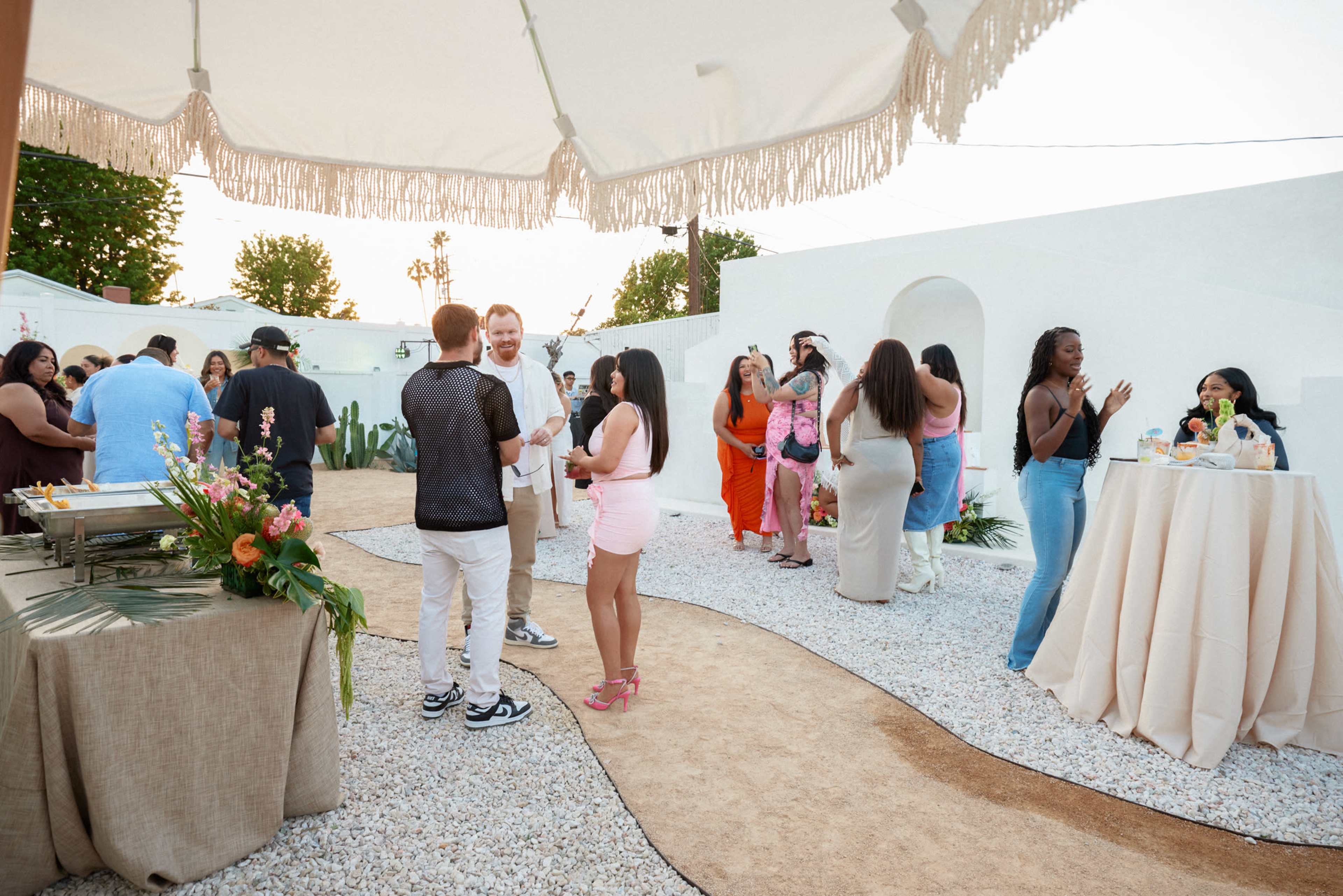 People socialize at an outdoor event in a garden setting with tables and decorations.