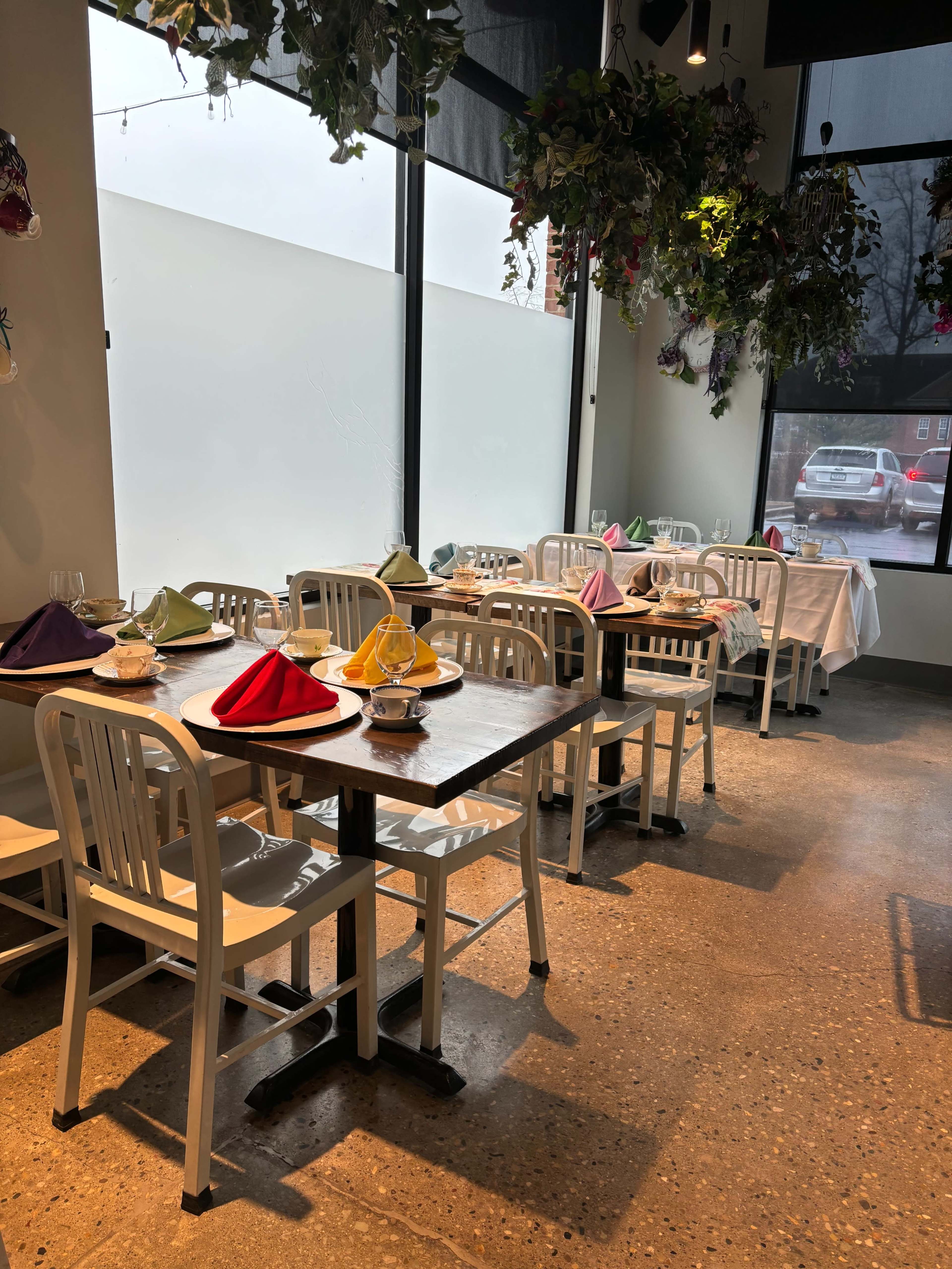 A dining area with white tables and chairs, each set with colored napkins, and adorned with hanging plants.