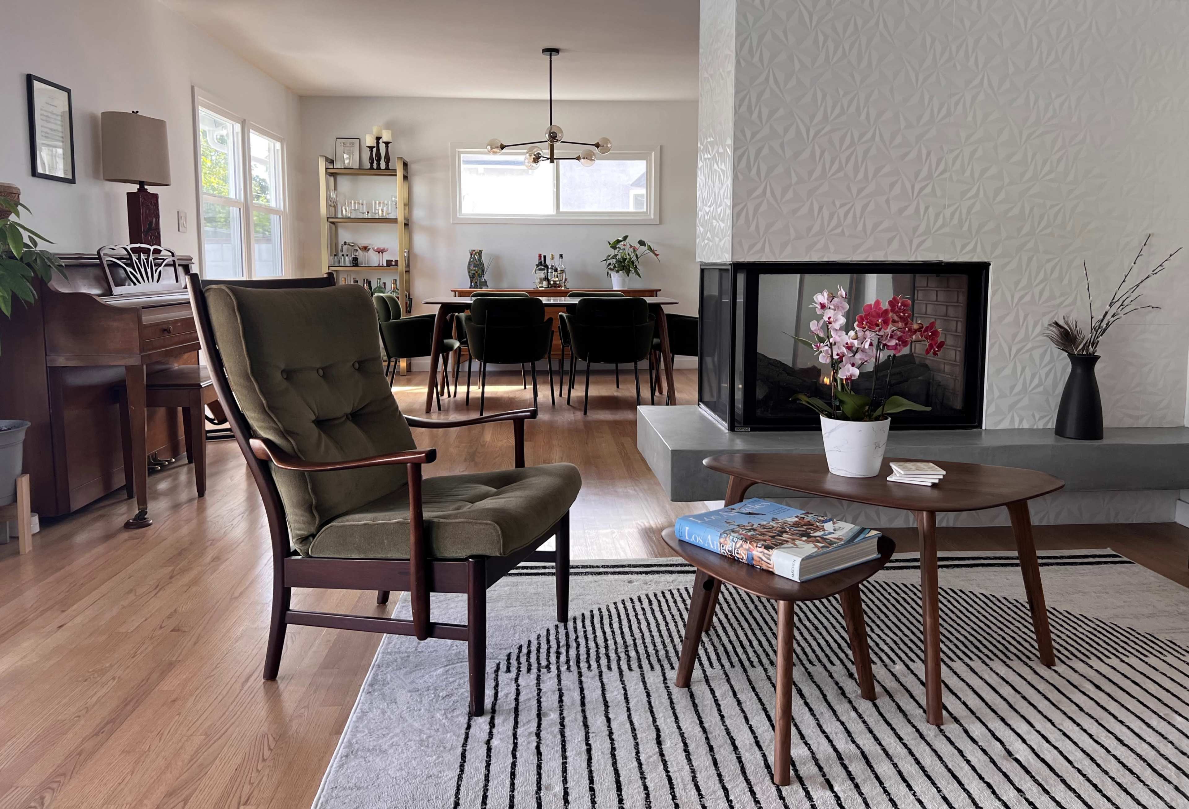 A modern living room with a green armchair, a wooden coffee table, and a fireplace, featuring a dining area in the background.