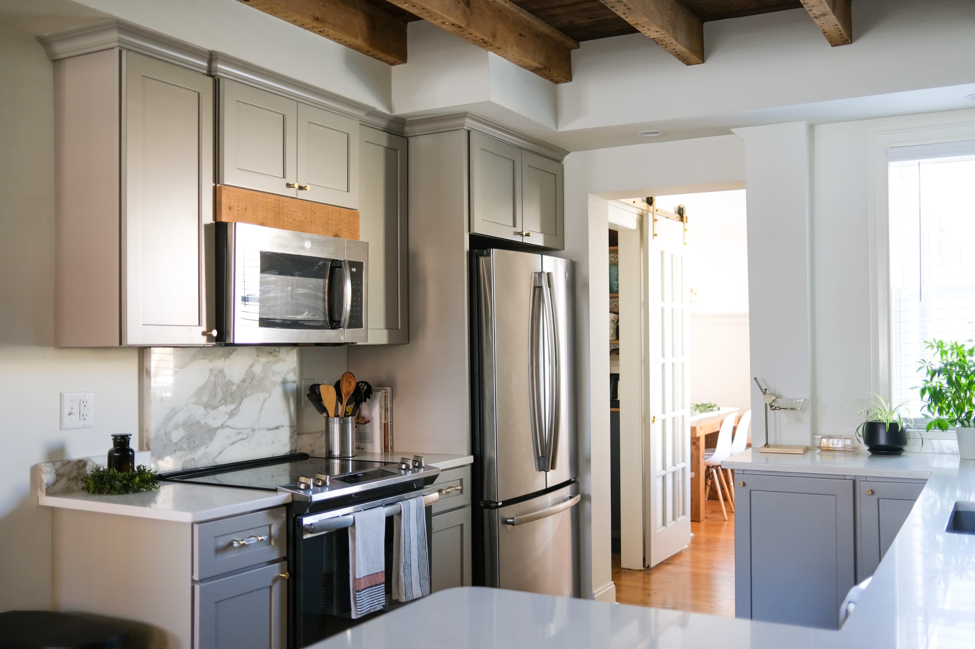 A modern kitchen with gray cabinets, stainless steel appliances, and a view into an adjacent dining area with a door framed by glass panels.