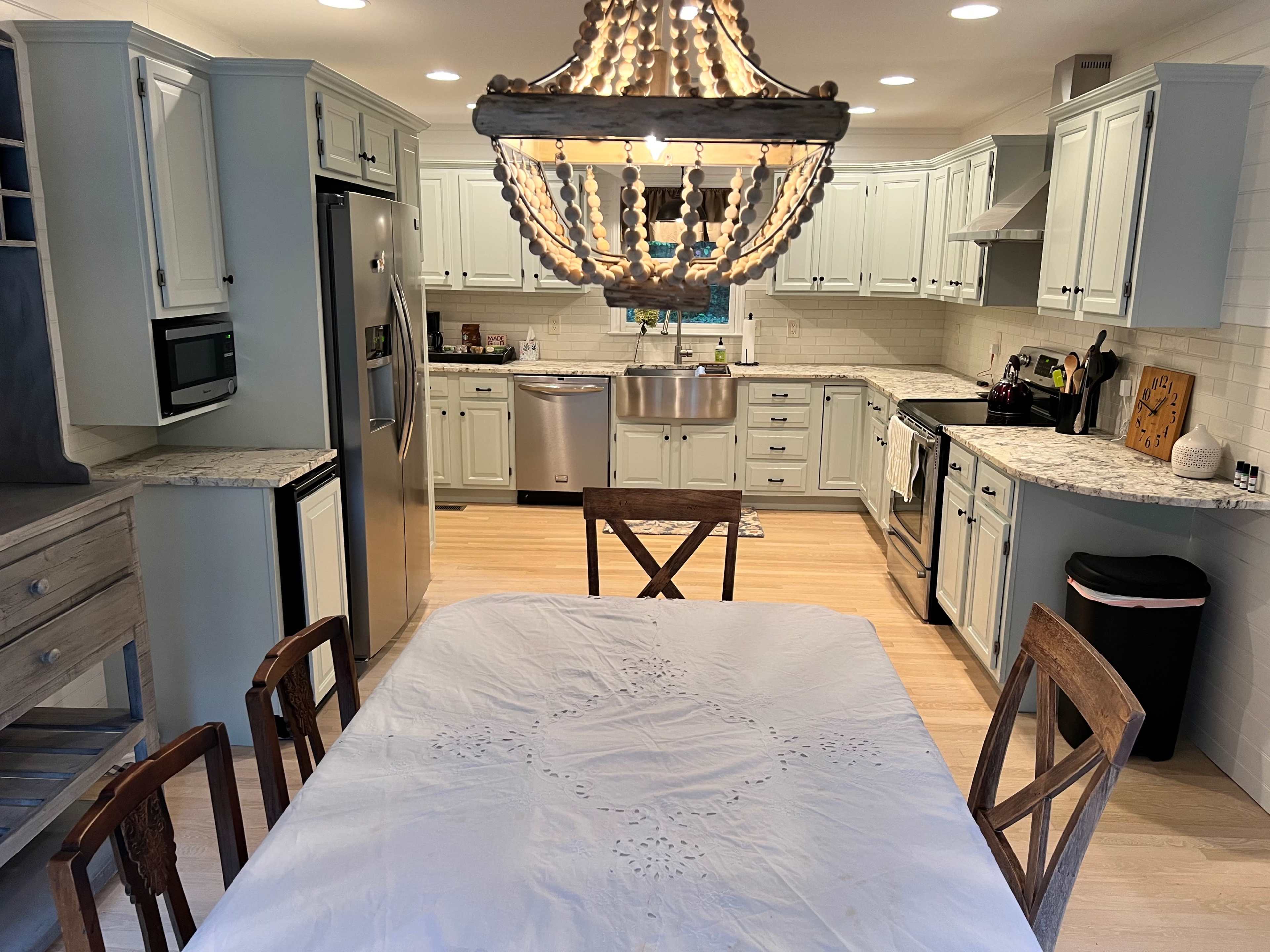A modern kitchen with light-colored cabinets, stainless steel appliances, and a dining table covered with a white tablecloth.