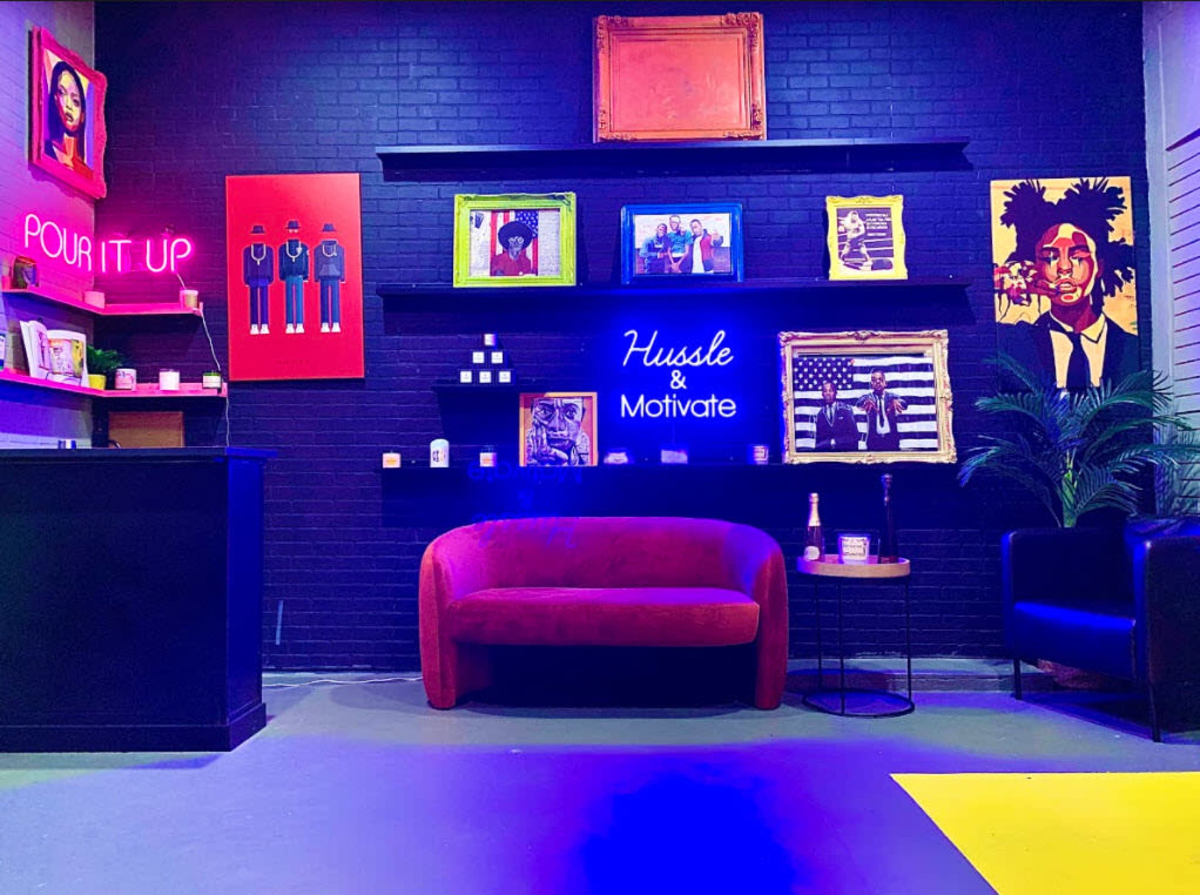 The scene features a modern lounge area with a red sofa, colorful artwork on the walls, and a neon sign that reads "Hustle & Motivate."