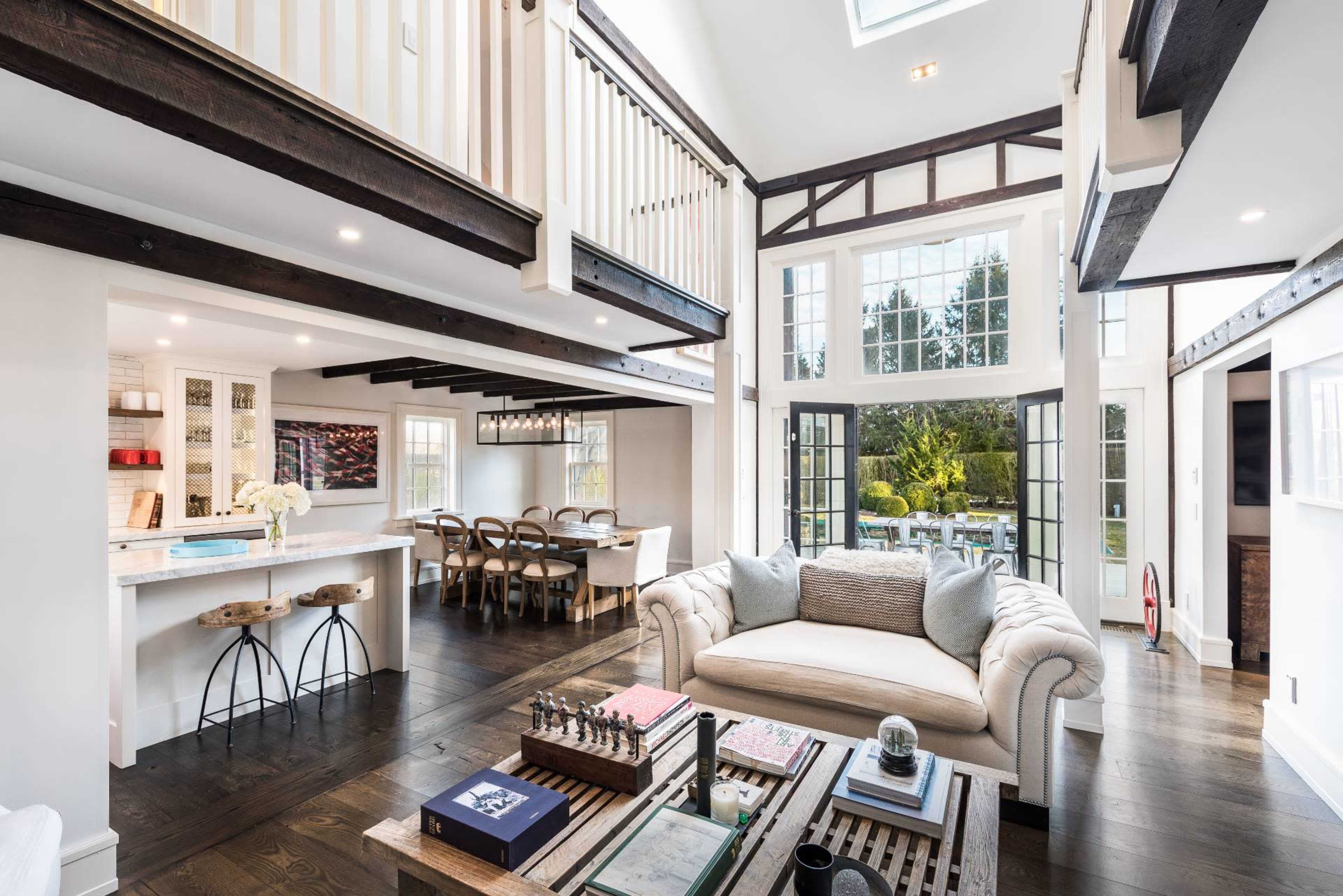 A modern open-concept living space with a white sofa, a coffee table with chess pieces, and large windows that open to a backyard.
