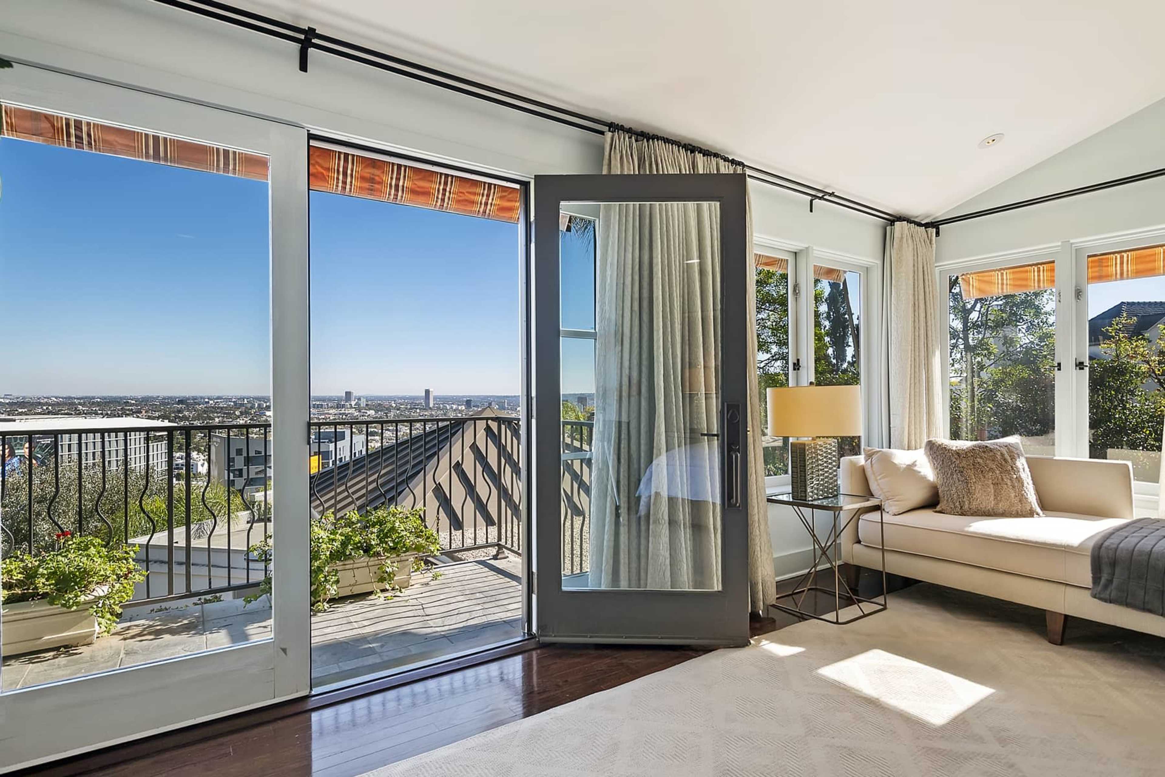 A bright room features large windows and a door opening to a terrace with a view of the city landscape.