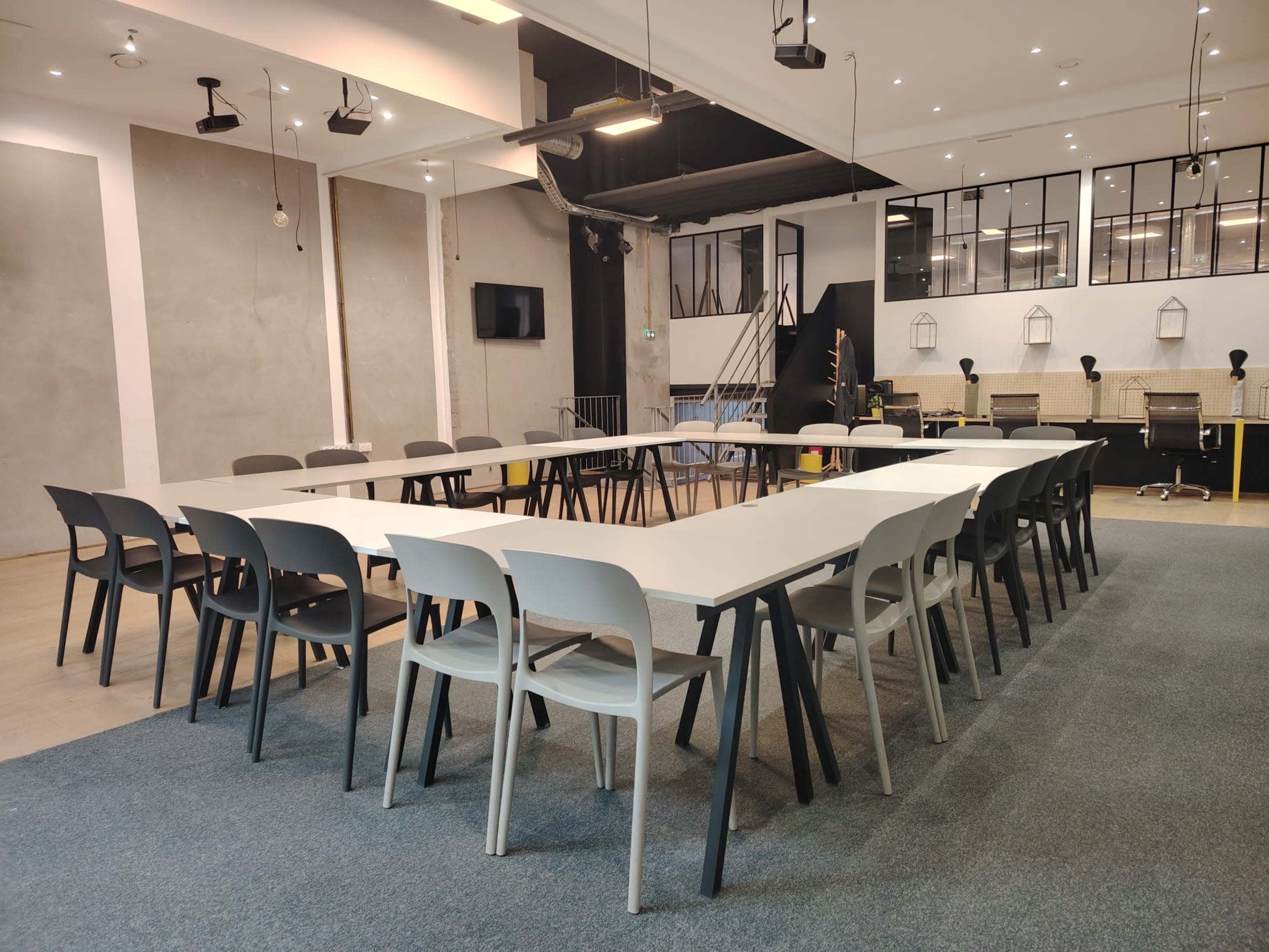 A spacious meeting room features a long table surrounded by chairs, with a modern design and large windows.