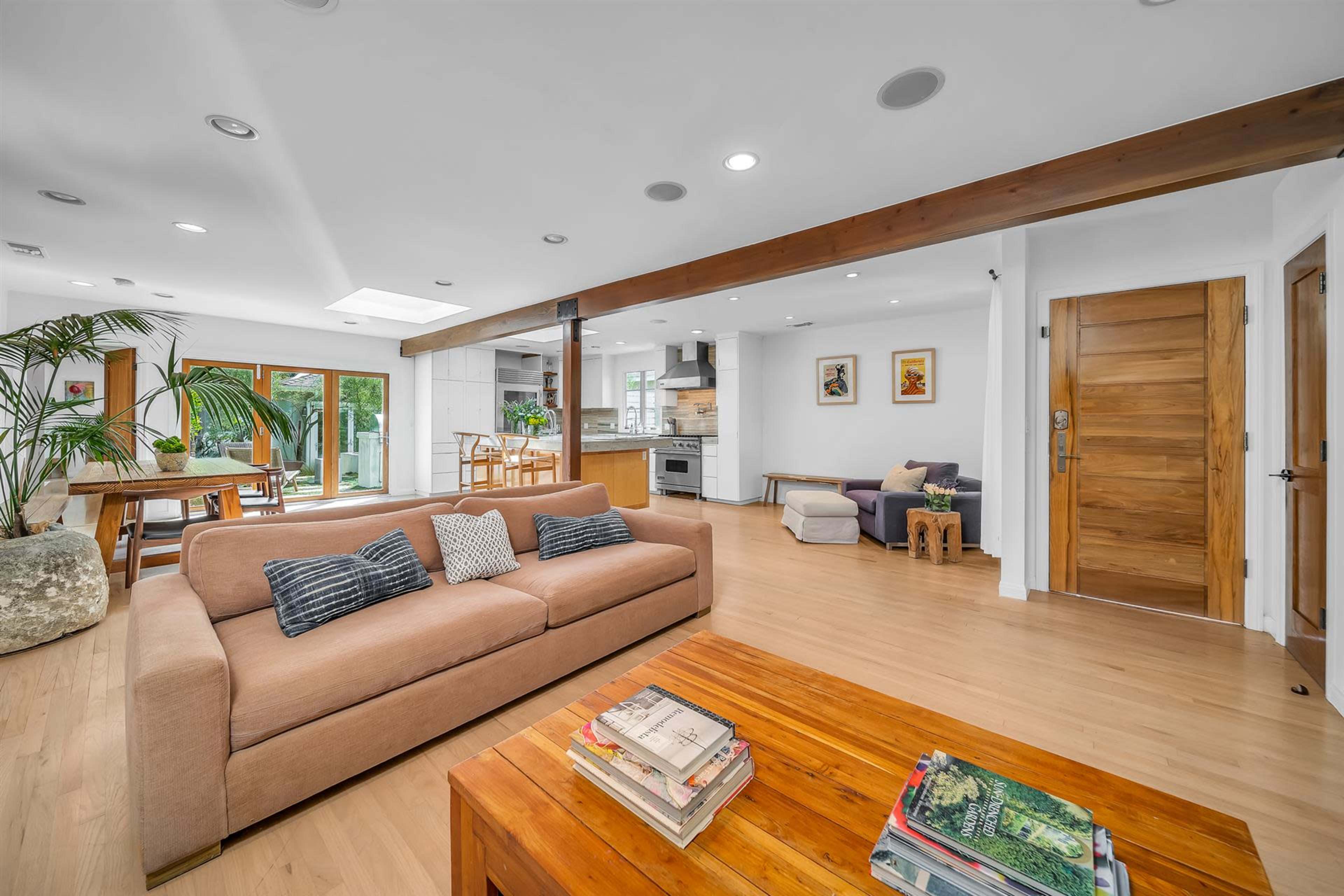 A modern, open living space featuring a sofa, wooden coffee table, and a dining area with large windows.
